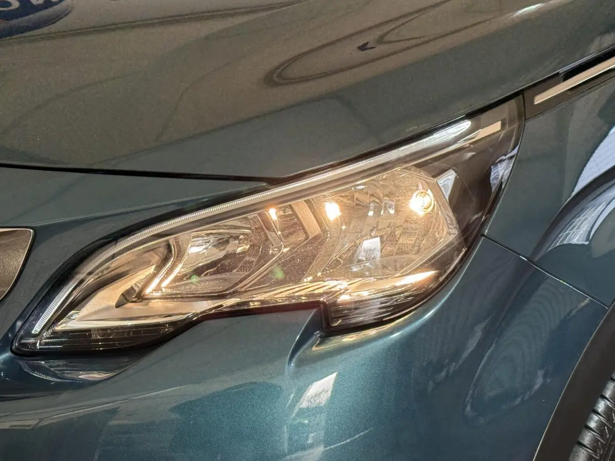 Gros plan sur le phare avant droit allumé d’un Peugeot 5008 bleu métallisé, version Puretech 130 S&S Allure.