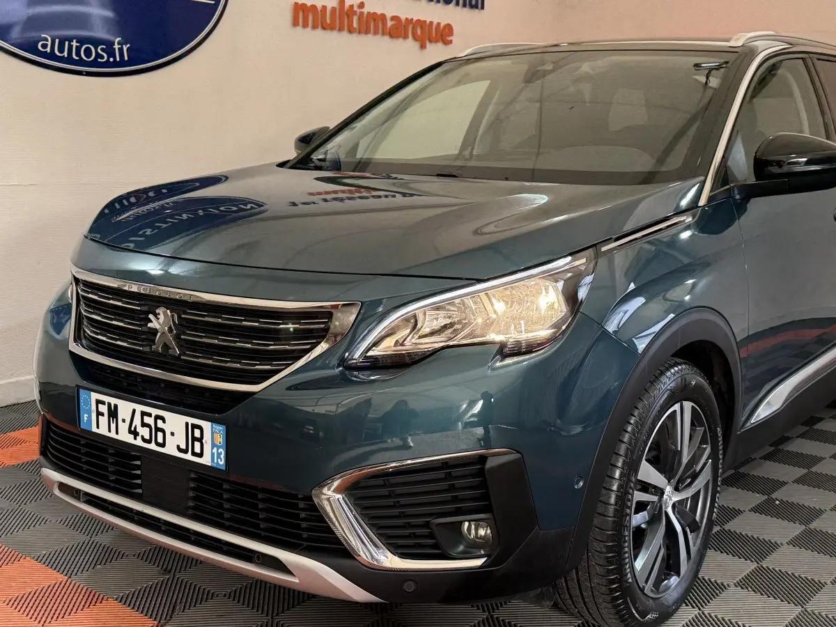 Vue 3/4 avant d’un Peugeot 5008 bleu métallisé avec phares allumés et jantes alliage distinctives.