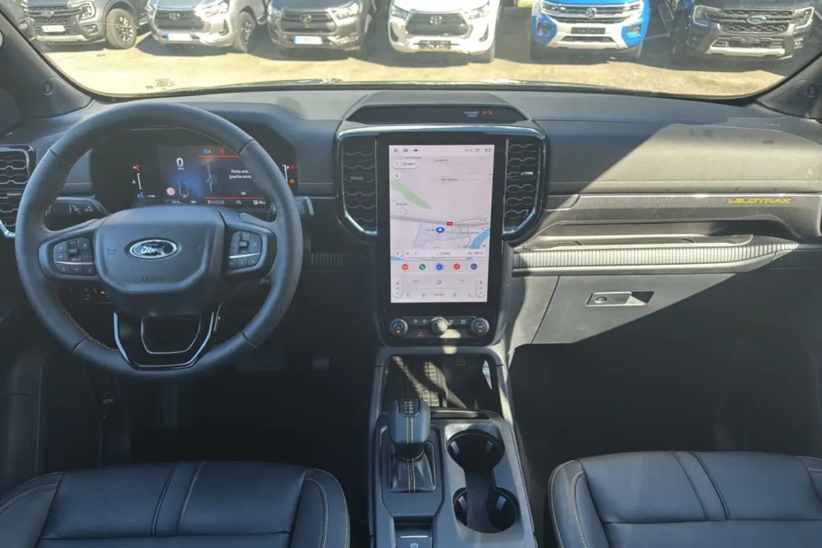 Vue intérieure avant du Ford Ranger Wildtrak 2025, tableau de bord noir avec écran tactile vertical et volant multifonctions.