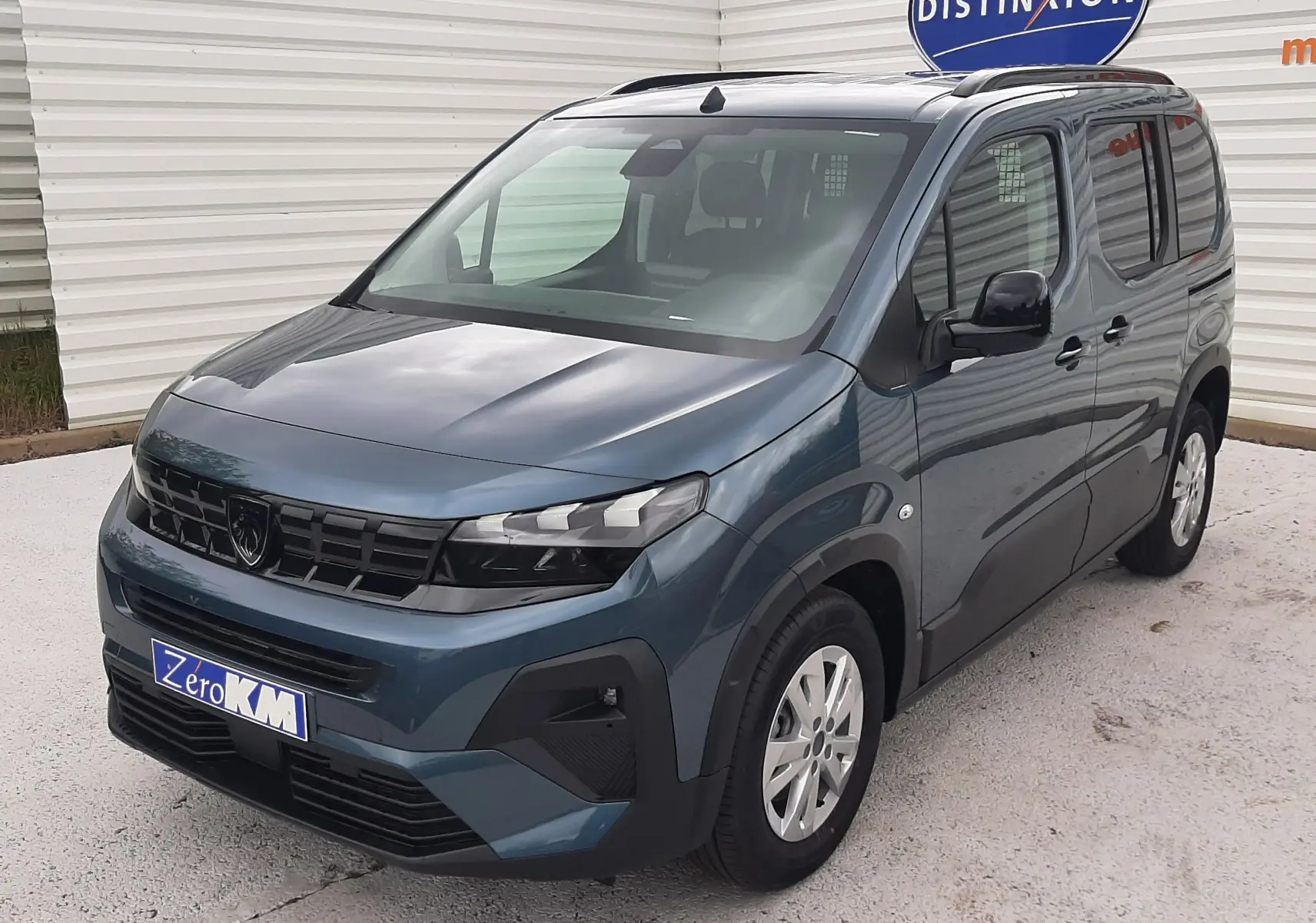 Peugeot Rifter bleu Kiama en 3/4 avant droit, avec calandre noire et jantes argentées, stationné devant un mur blanc.