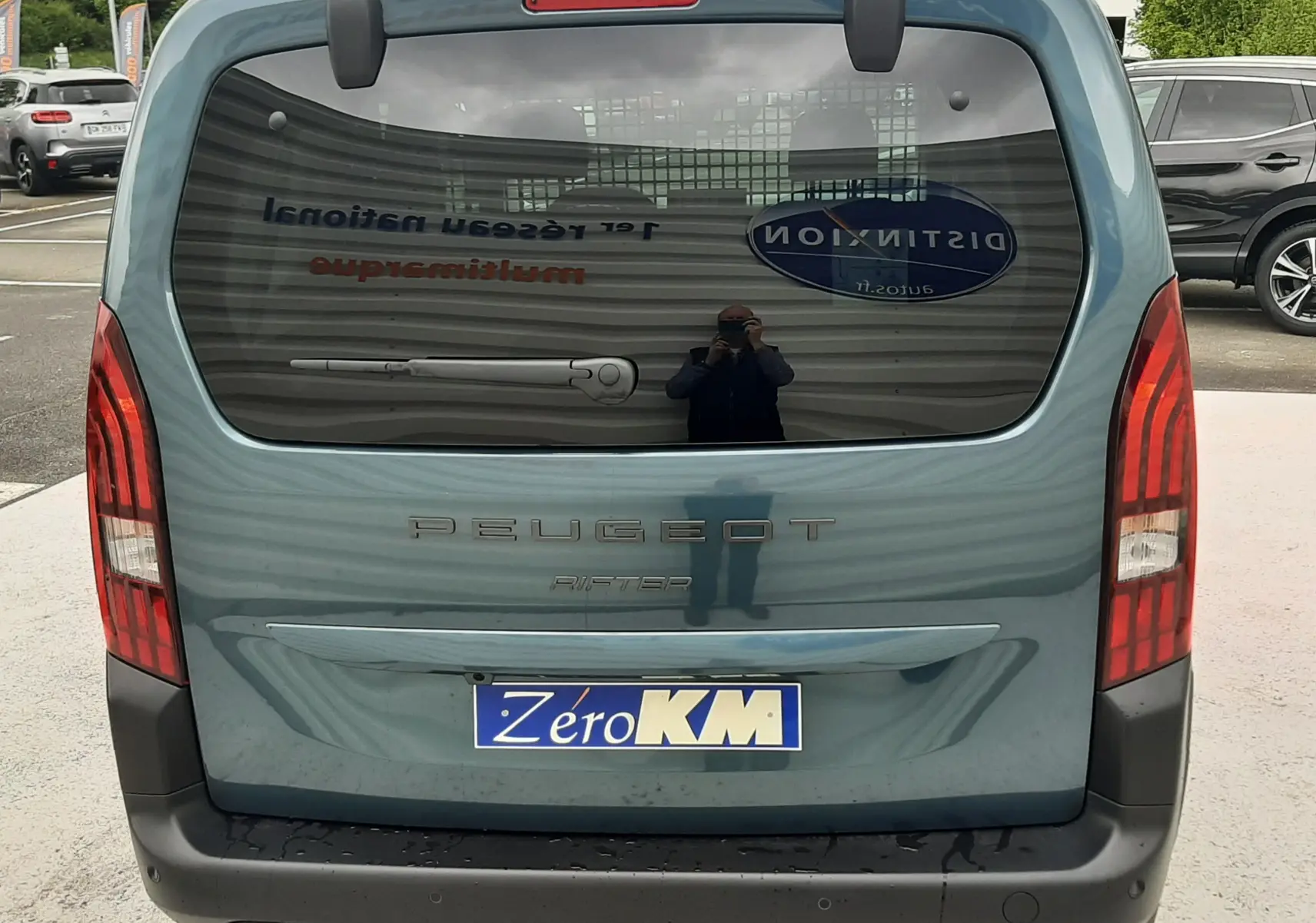 Vue arrière d'un Peugeot Rifter bleu Kiama 2026 avec hayon vitré et feux arrière verticaux rouges.