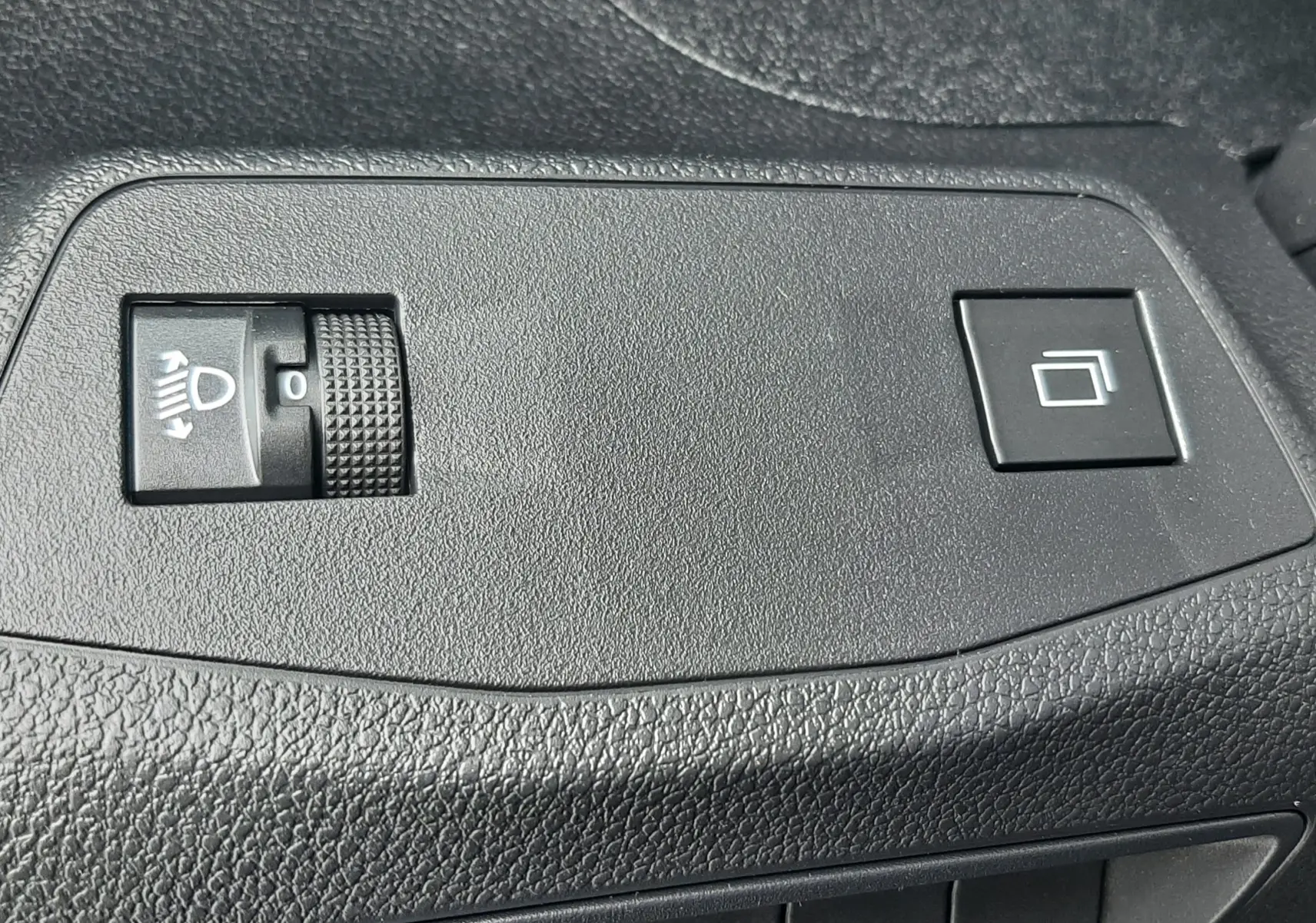Gros plan sur les commandes noires du tableau de bord intérieur du Peugeot Rifter bleu Kiama, boutons de réglage des phares et fonction tactile.