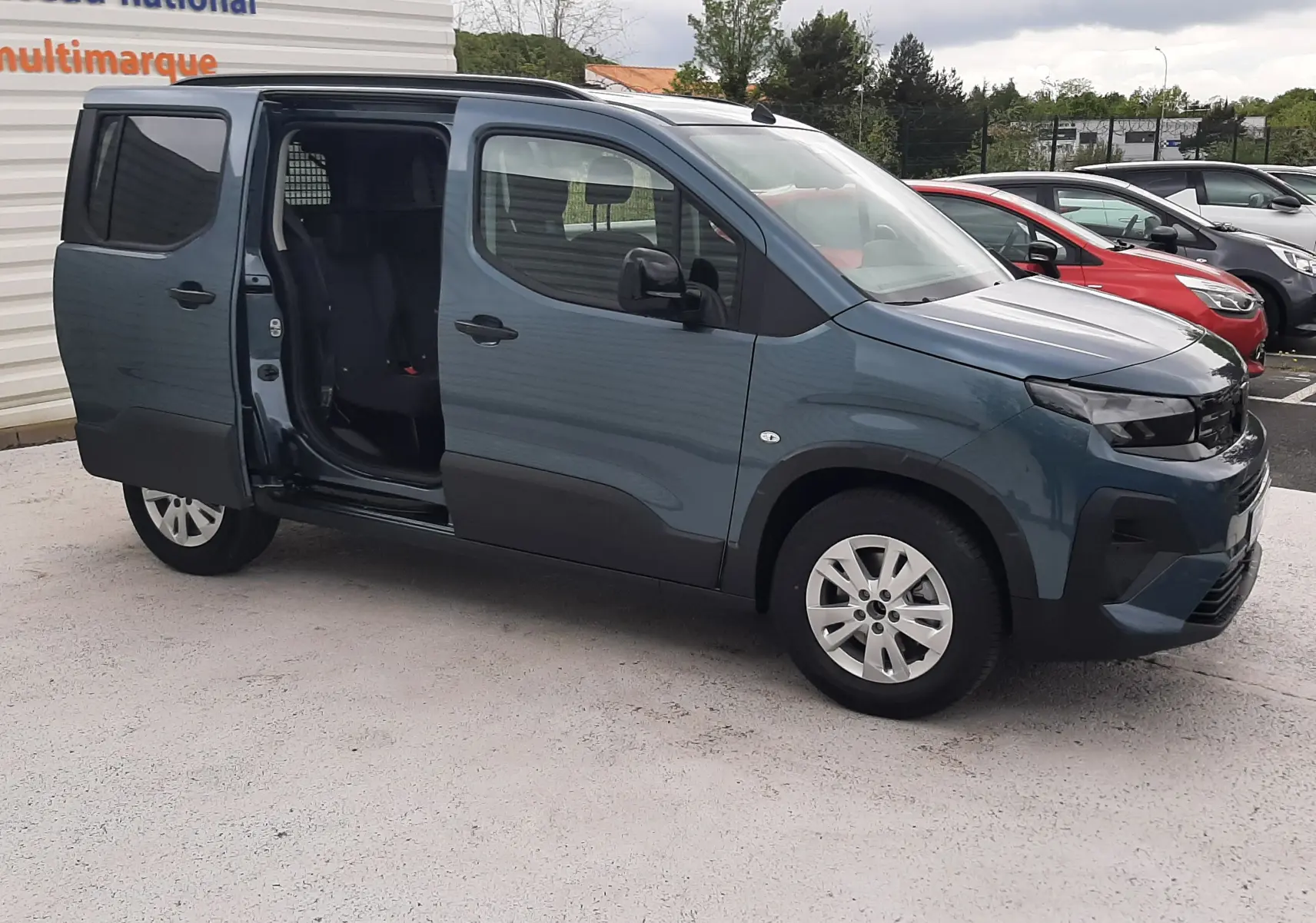 Peugeot Rifter bleu Kiama vu de profil droit avec porte coulissante arrière ouverte sur parking.