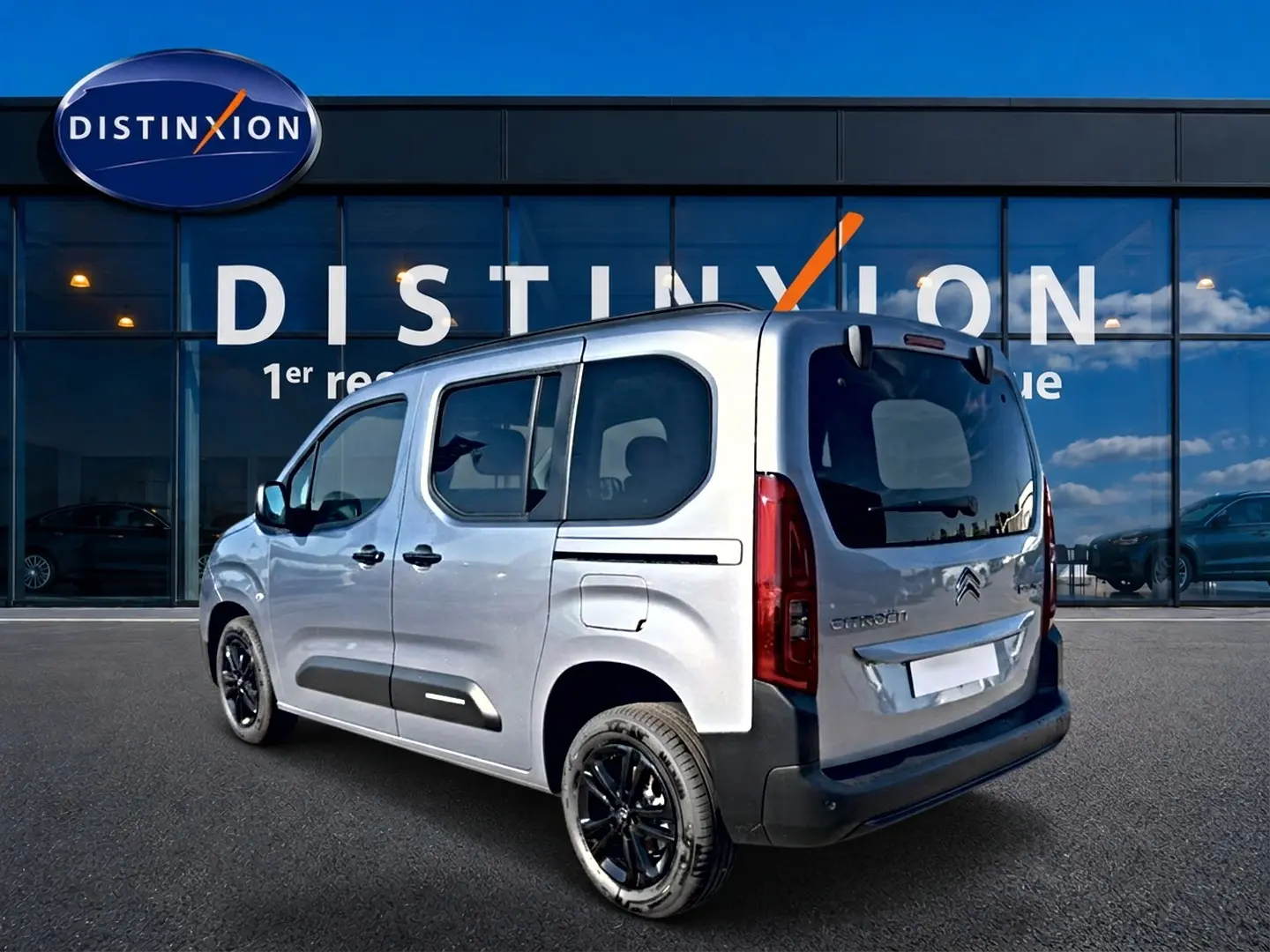 Vue 3/4 arrière droite d'un Citroën Berlingo gris acier avec jantes noires, portes latérales vitrées et logo visible.