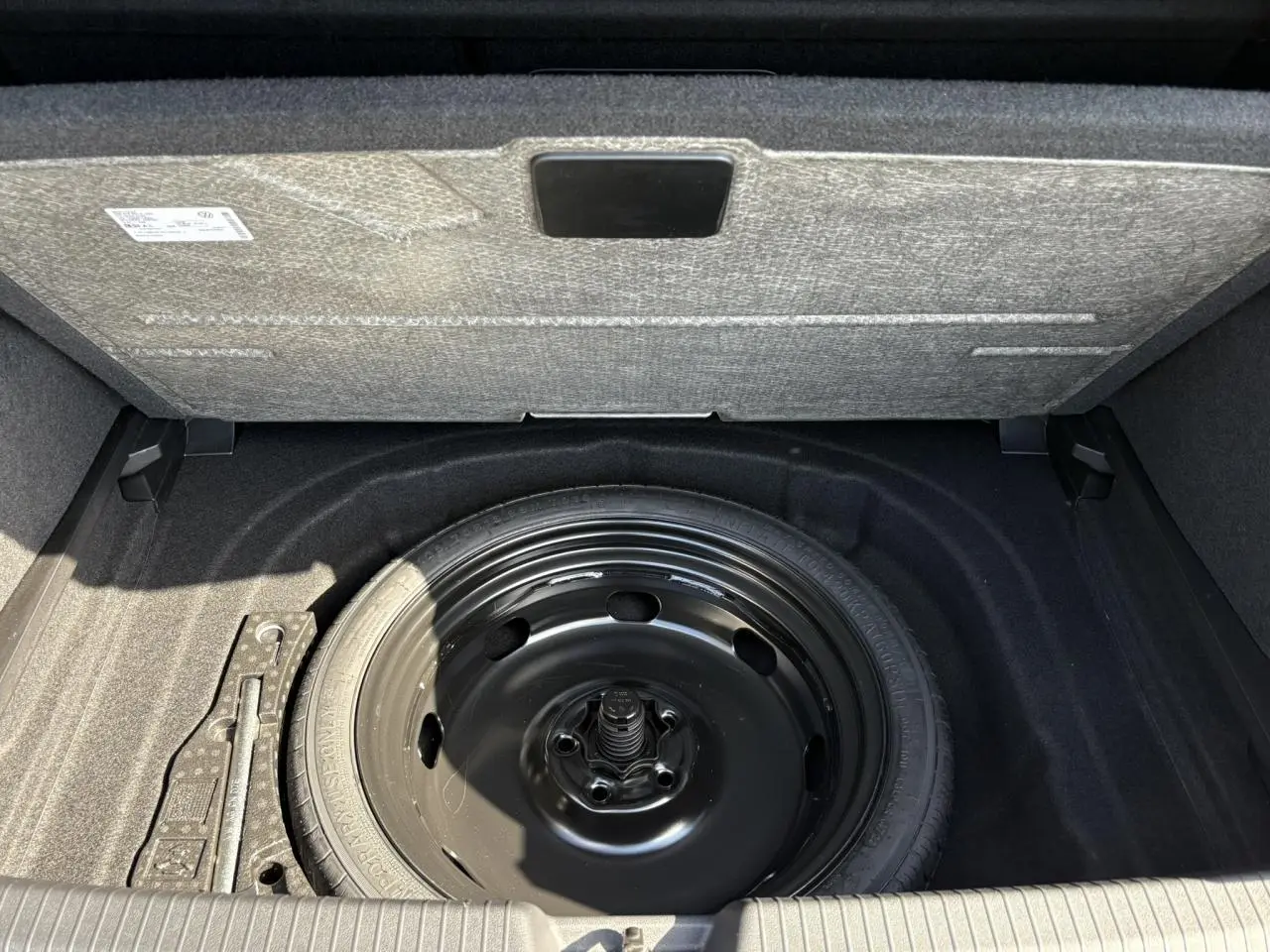 Vue plongeante sur la roue de secours noire dans le coffre d'une Volkswagen Golf VIII 1.5 TSI gris lunaire 2024.