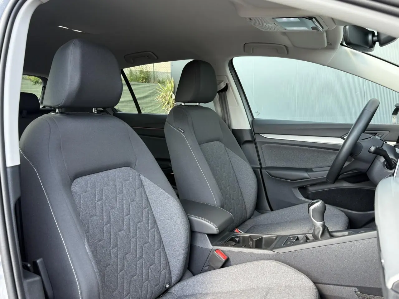 Vue intérieure côté conducteur de la Volkswagen Golf VIII 1.5 TSI 150 Active avec sièges tissu gris et volant multifonction.