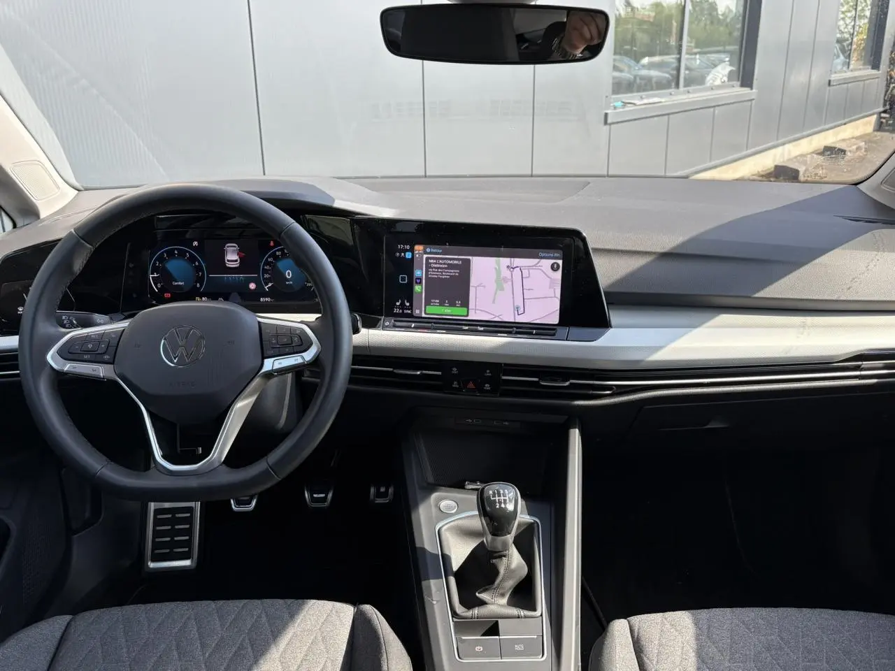 Vue intérieure de la Volkswagen Golf VIII 1.5 TSI 2024 montrant le volant multifonction, tableau de bord numérique et levier de vitesses manuel.