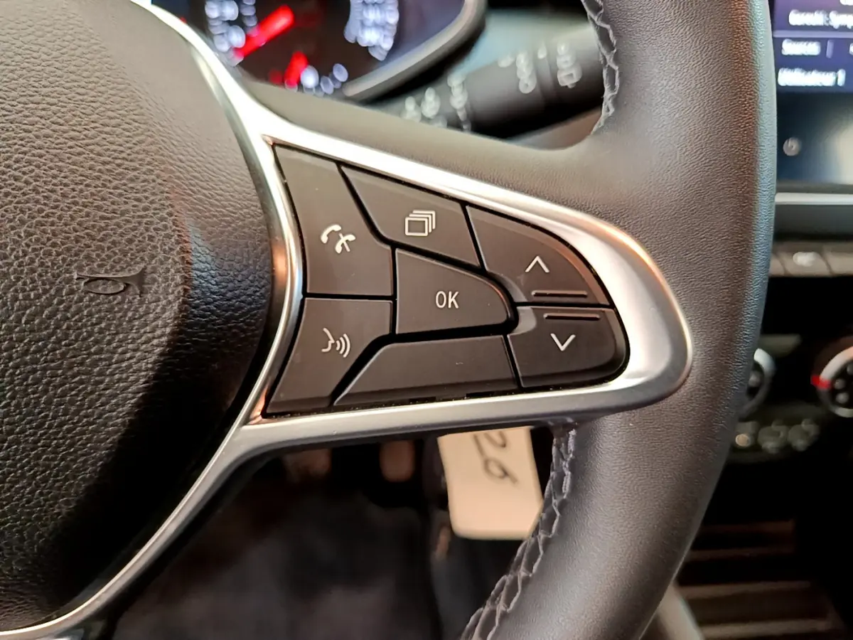 Gros plan sur les commandes multifonctions du volant cuir noir de la Renault Clio Business blanche de 2021.