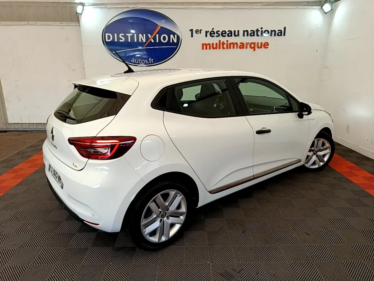 Vue 3/4 arrière droite d'une Renault Clio Business blanche, avec jantes alliage et feux arrière LED visibles dans un showroom.