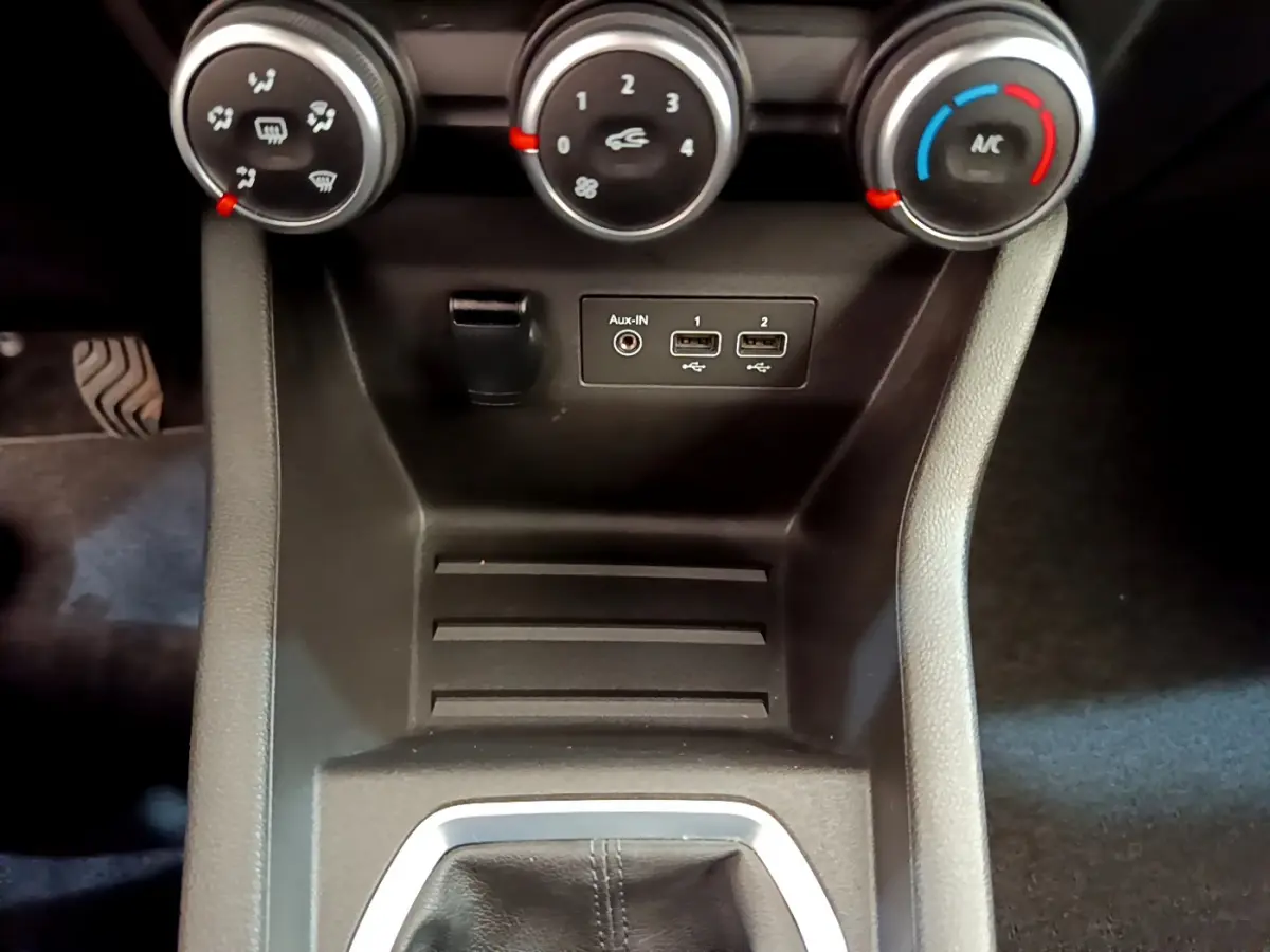 Vue rapprochée du tableau de bord central de la Renault Clio Business blanc, avec commandes de climatisation et ports USB visibles.