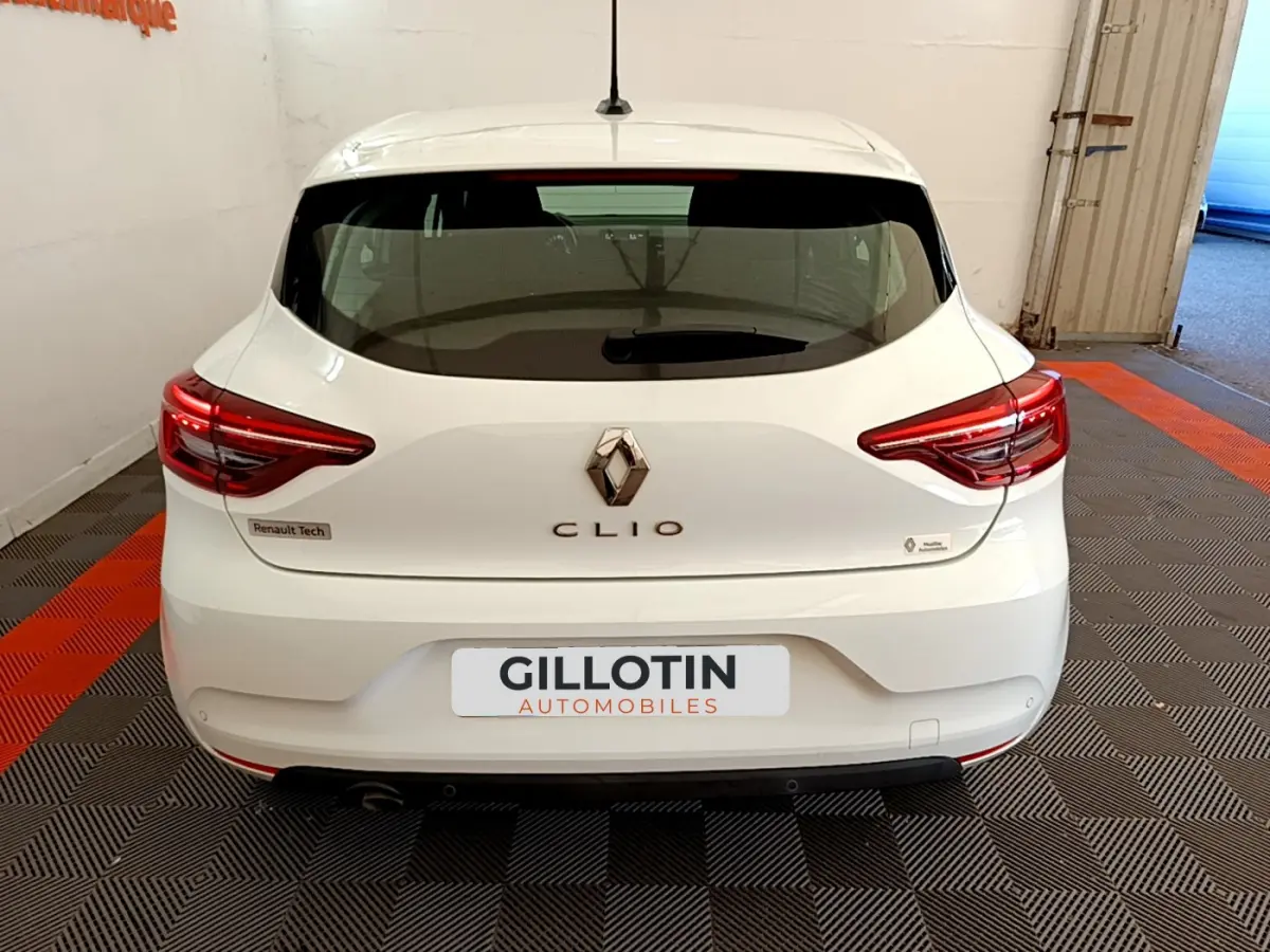Vue arrière d'une Renault Clio blanche 2021 avec feux LED et logo Renault bien visibles dans un garage.