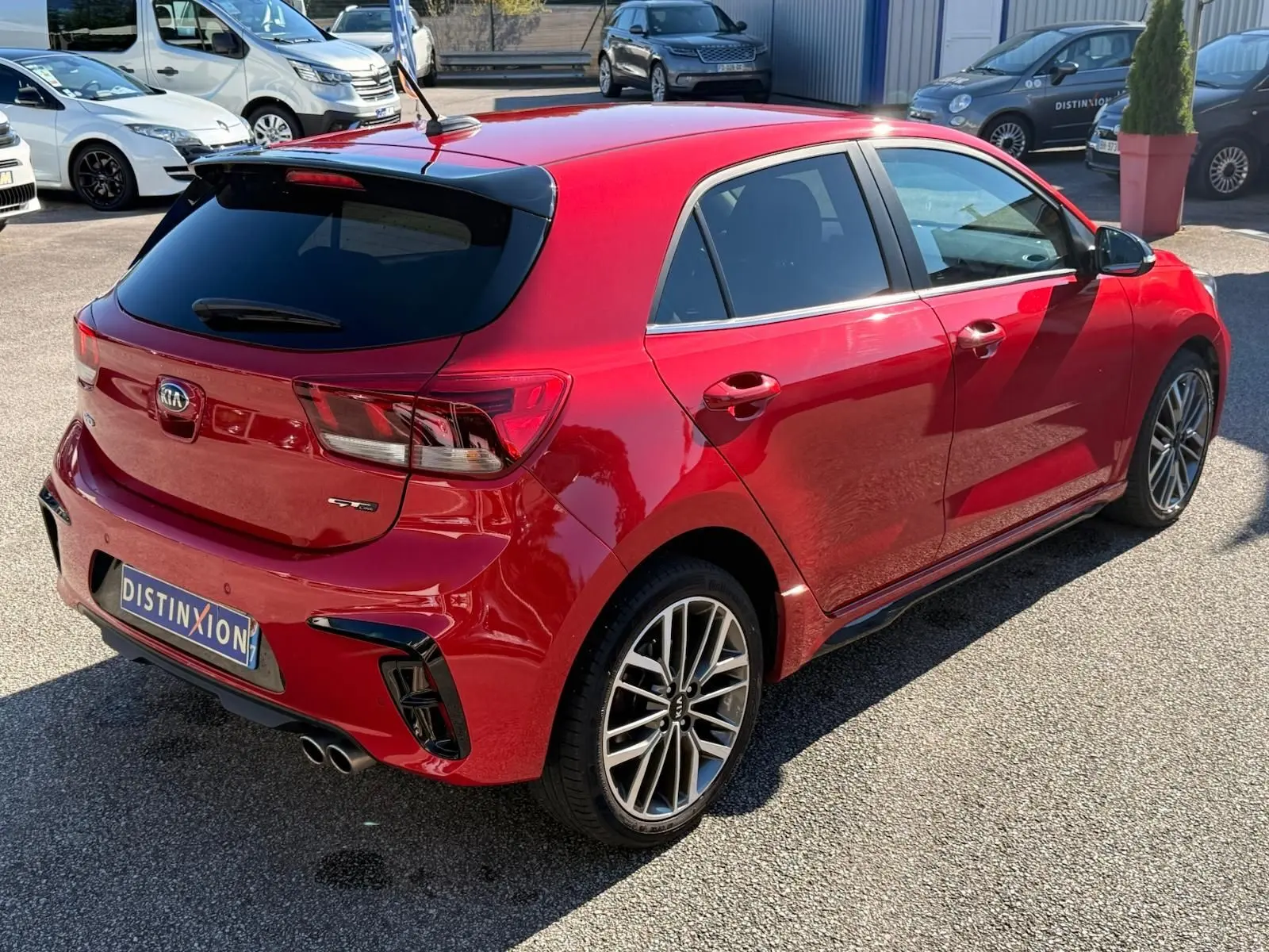 Vue 3/4 arrière droite d'une KIA RIO GT-LINE rouge grenadine avec jantes alliage et double sortie d'échappement chromée.