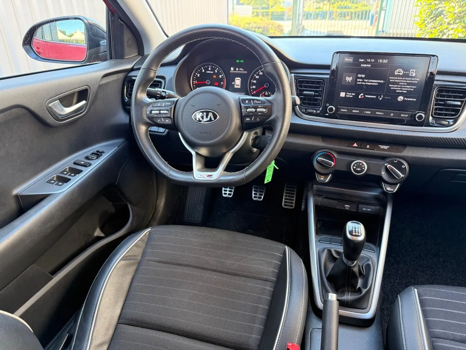 Vue intérieure côté conducteur de la KIA RIO rouge grenadine 2022, volant multifonction et boîte manuelle visibles.