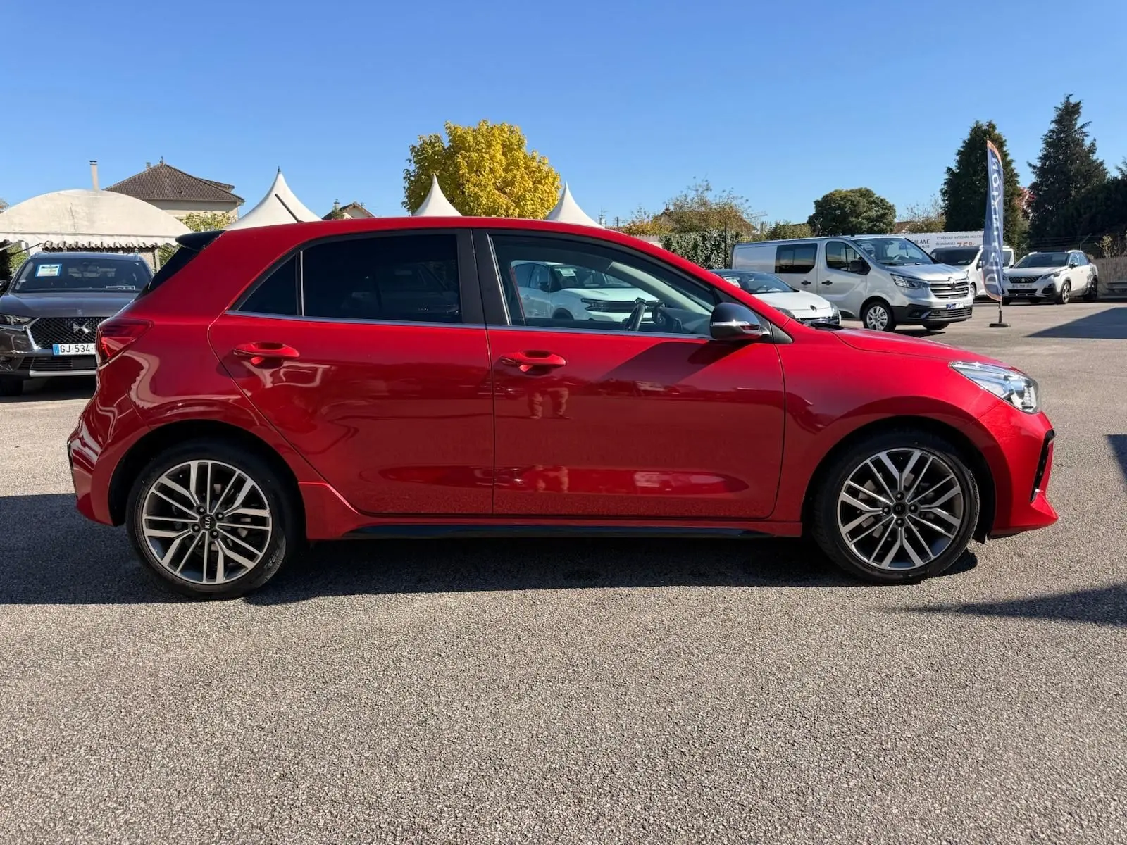 Profil côté gauche d'une KIA RIO rouge grenadine 2022, version GT-LINE, avec jantes alliage et vitres teintées.
