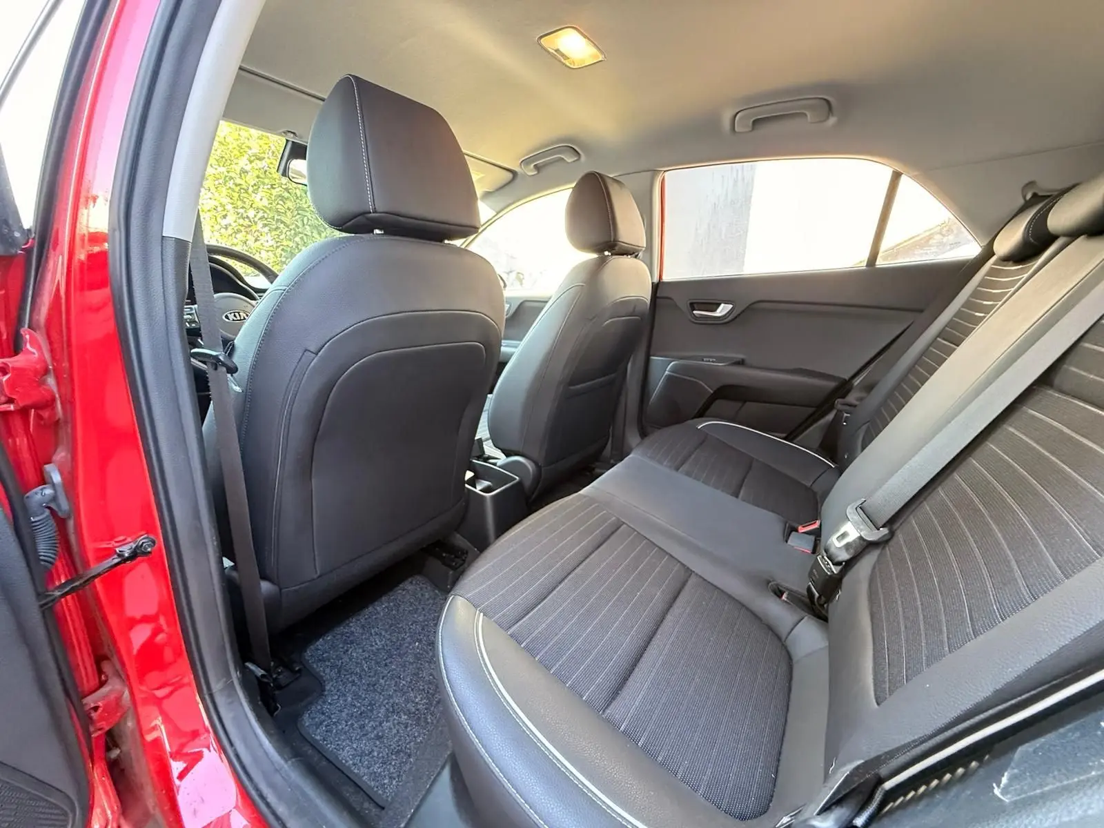 Vue intérieure arrière droit de la Kia Rio rouge grenadine 2022, sièges noirs en tissu et cuir avec ceinture de sécurité.