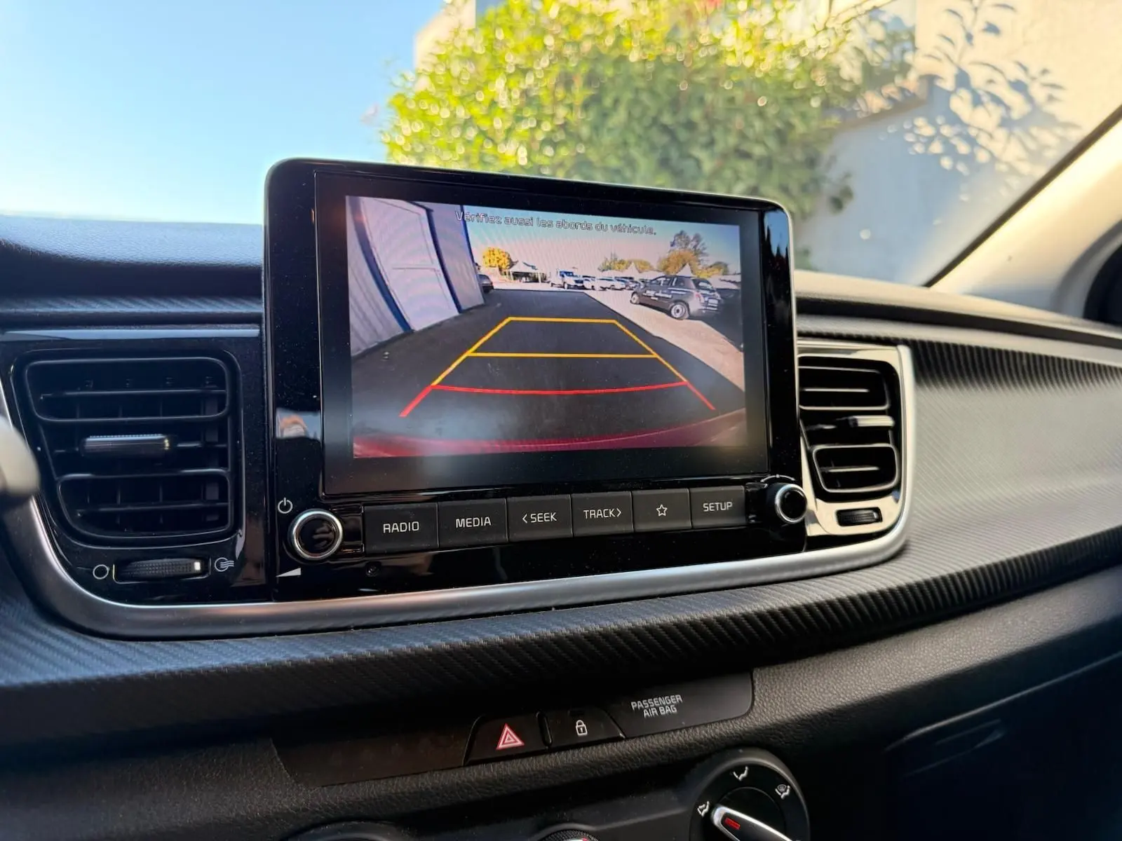Écran central de la Kia Rio rouge grenadine 2022 montrant la caméra de recul avec guidage de trajectoire en jaune et rouge.