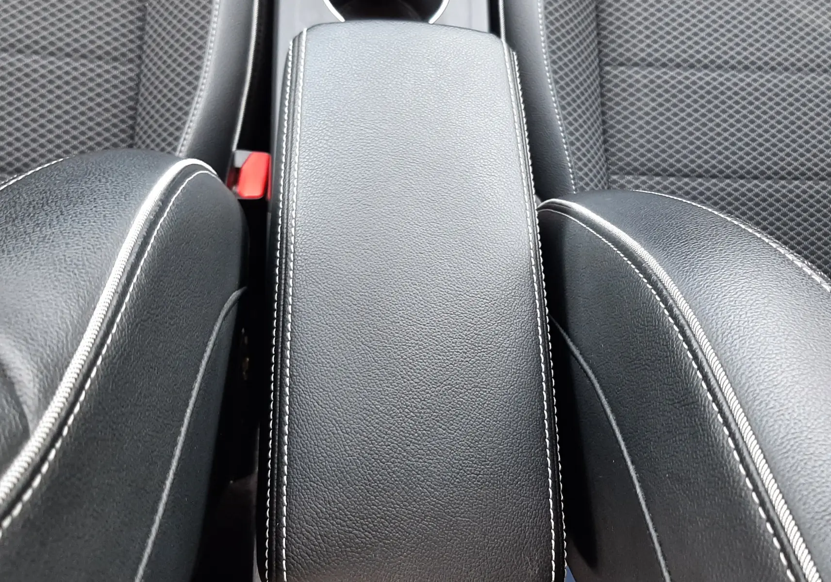 Vue plongeante sur l'accoudoir central en cuir noir avec surpiqûres blanches entre les sièges avant en tissu gris du Renault Arkana.
