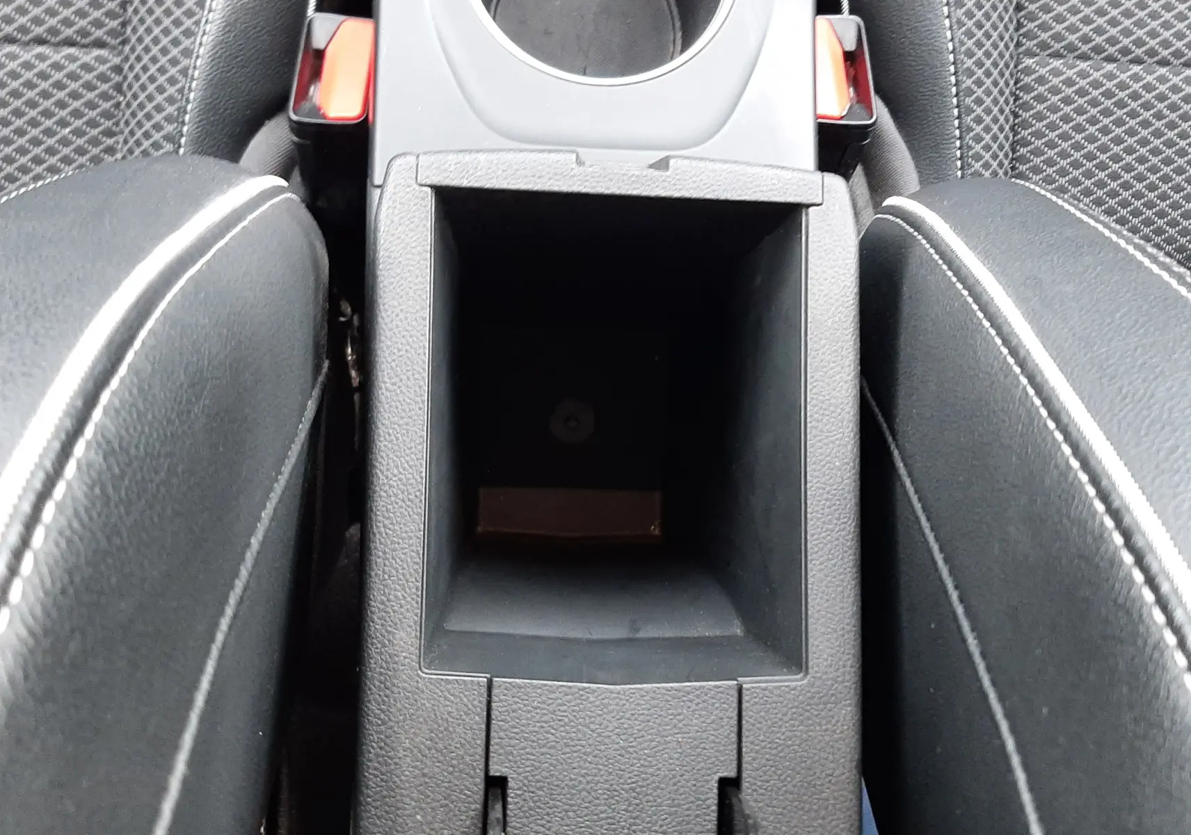 Vue plongeante sur la console centrale noire avec rangement ouvert et accoudoirs en cuir noir à surpiqûres blanches du Renault Arkana.