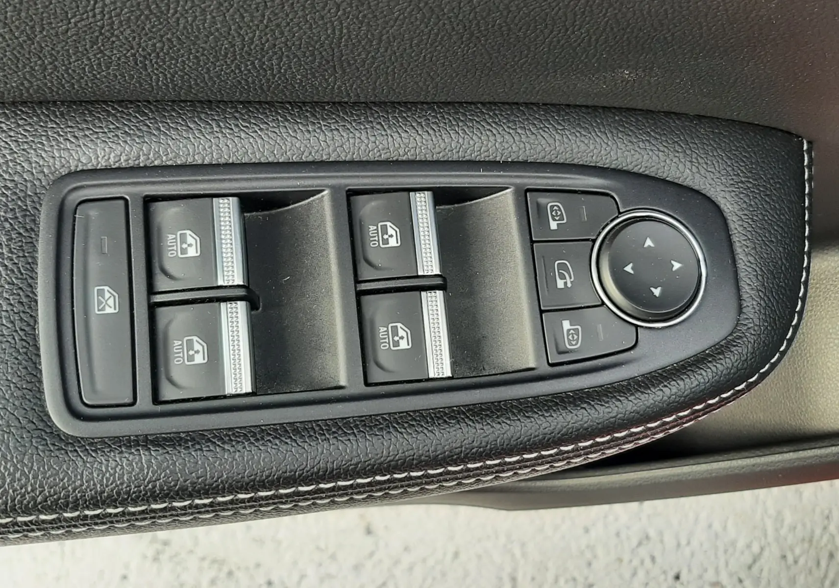 Gros plan sur les commandes de lève-vitres et rétroviseurs côté gauche en cuir noir avec surpiqûres blanches dans une Renault Arkana rouge Flame.