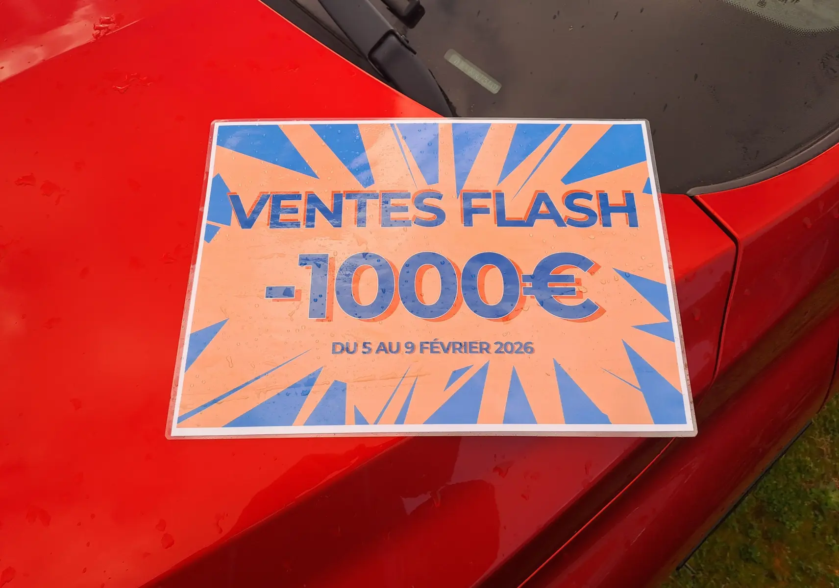 Vue rapprochée du capot rouge flame d'une Renault Arkana 2021 avec une affiche de promotion "Ventes Flash -1000€".