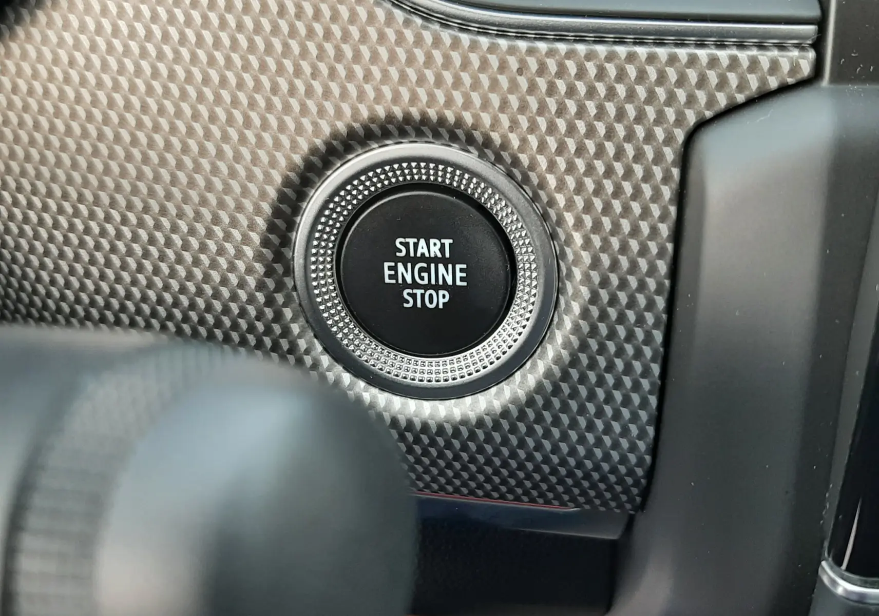 Gros plan sur le bouton Start Engine Stop entouré d’un habillage à motif carbone dans le Renault Arkana rouge Flame 2021.