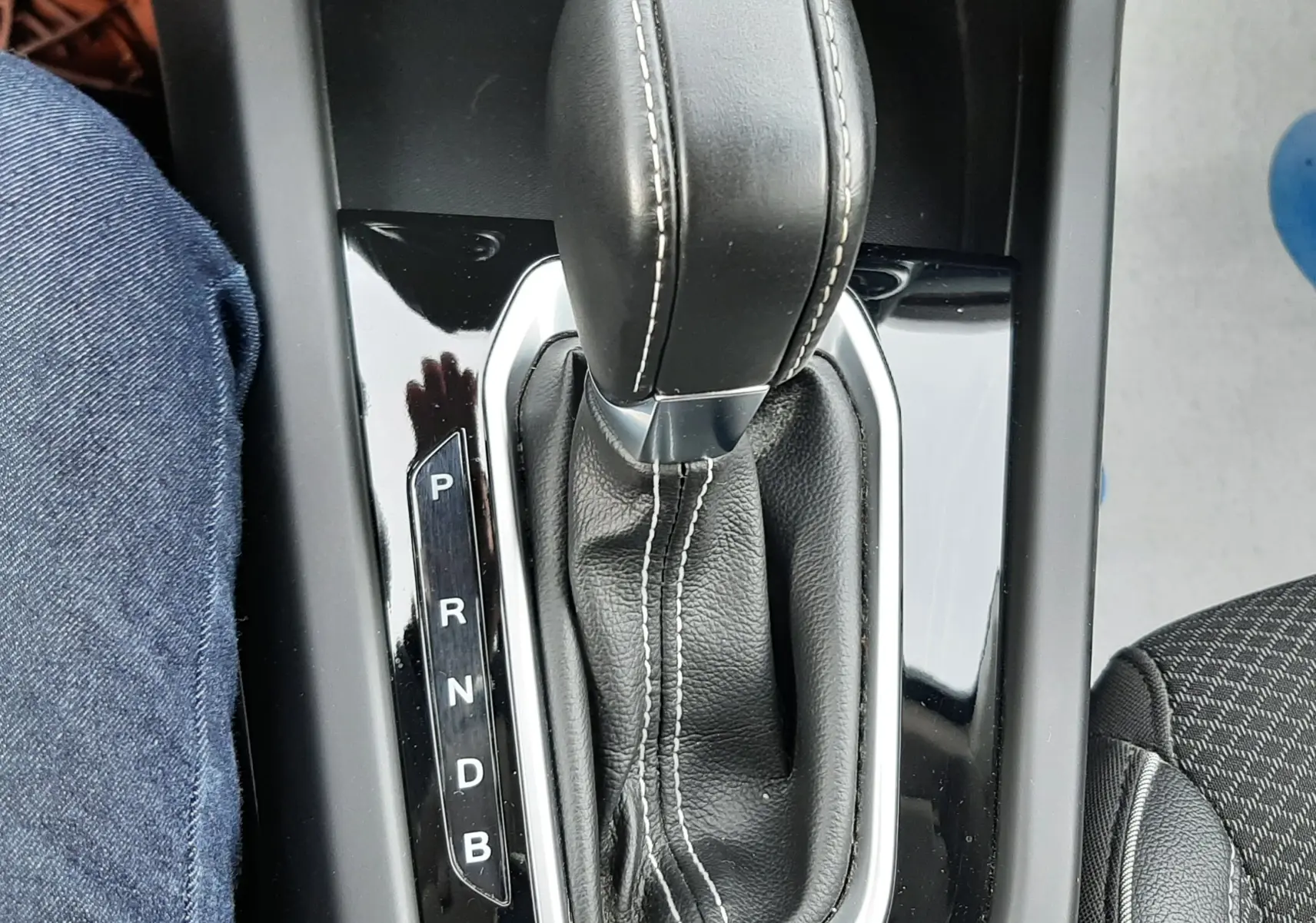 Gros plan sur la commande de la boîte automatique en cuir noir avec surpiqûres blanches dans un Renault Arkana Rouge Flame.