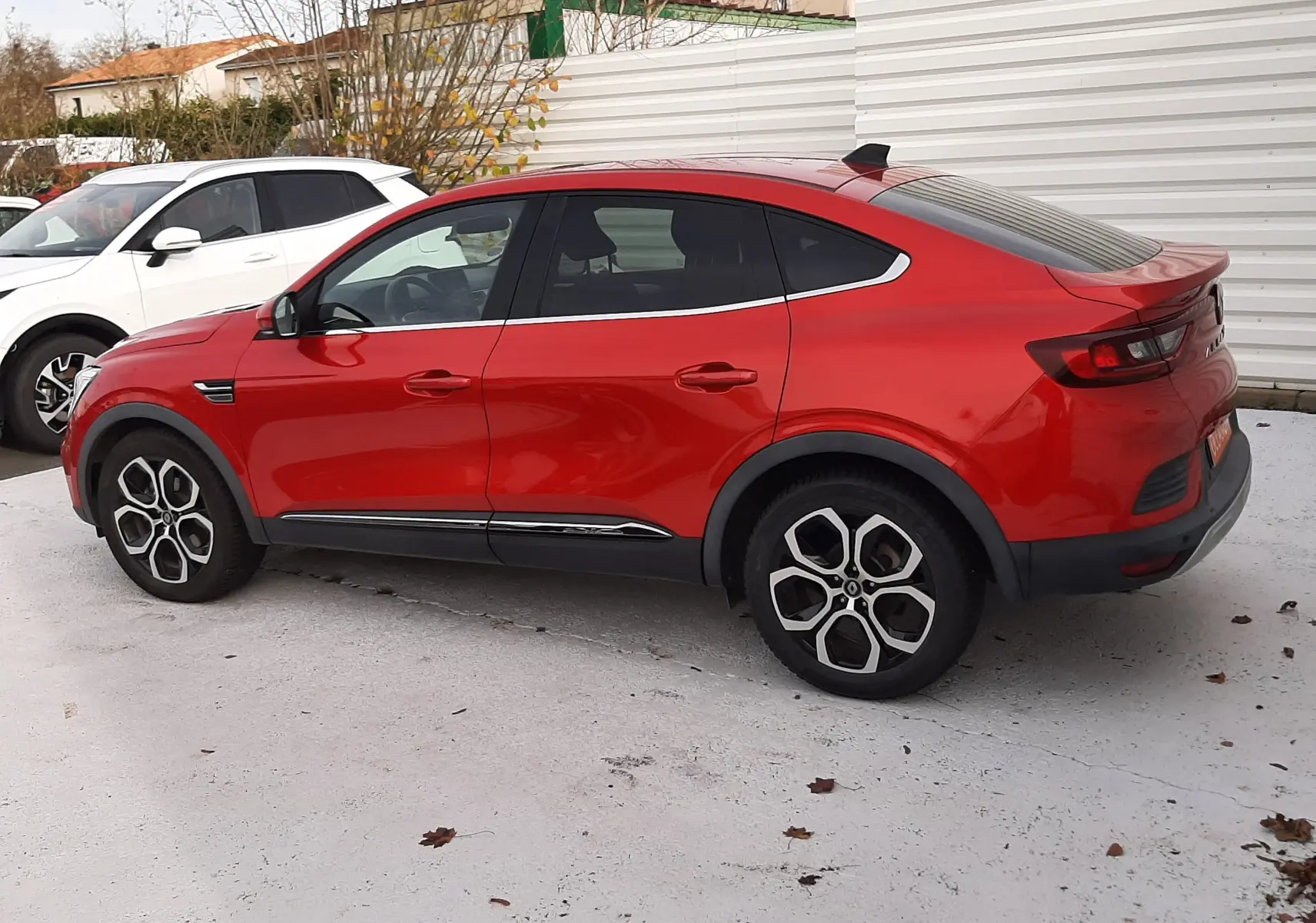 Vue de profil côté gauche d'un Renault Arkana rouge Flame avec toit plongeant et jantes distinctives.