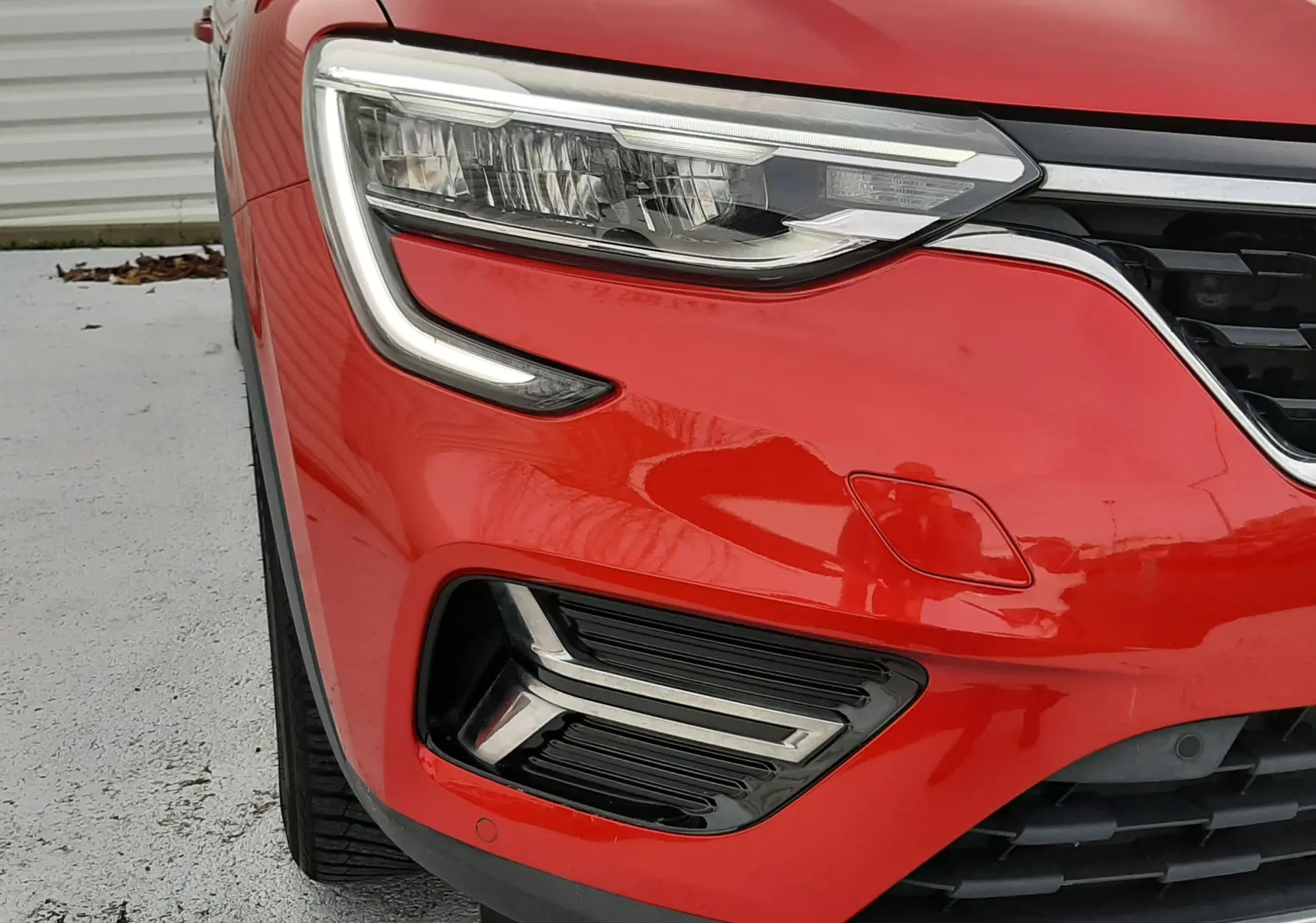 Gros plan sur l'avant gauche rouge flame du Renault Arkana 1.6 E-TECH 145 avec feux LED distinctifs et calandre noire.