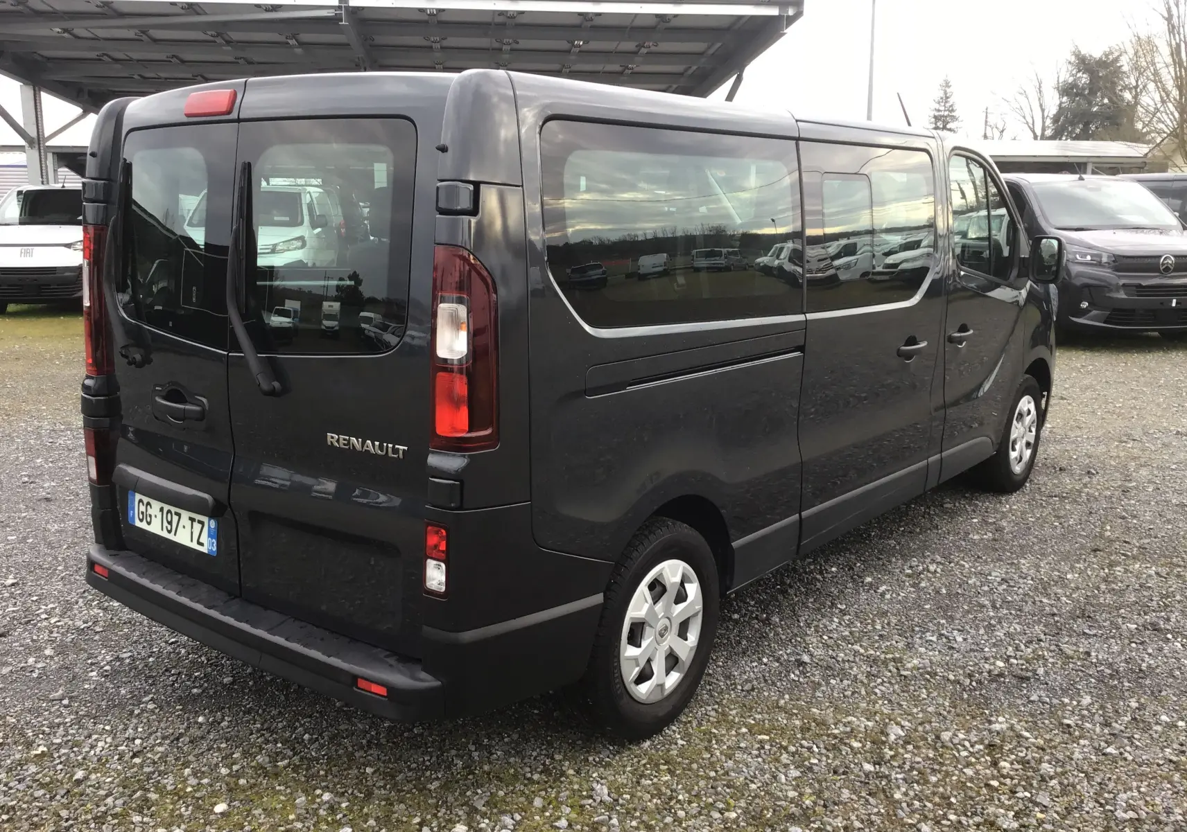 Vue 3/4 arrière droite d’un Renault Trafic Combi gris comète avec vitres latérales teintées et portes arrière battantes.