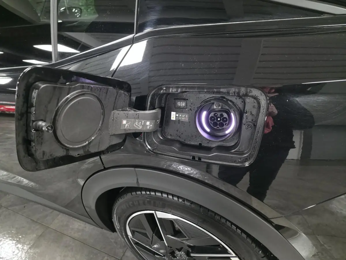 Prise de recharge ouverte côté gauche arrière d’une Peugeot 408 noire, avec jante alliage 19 pouces visible.