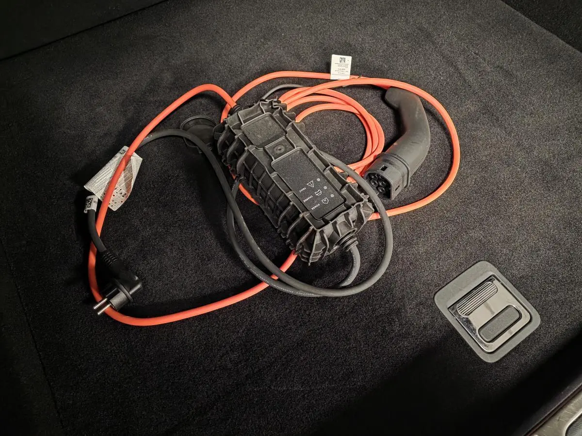 Câble de recharge orange et noir posé sur le tapis noir du coffre d'une Peugeot 408 hybride rechargeable 2024.