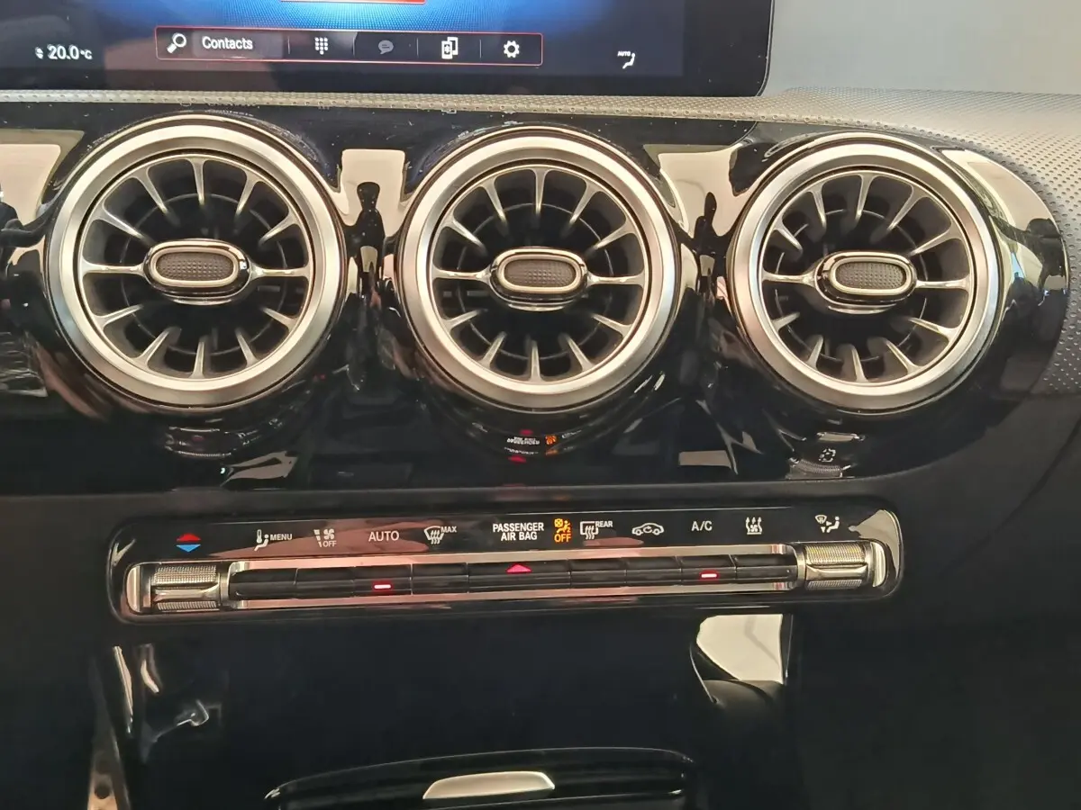 Détail intérieur montrant les trois aérateurs ronds chromés et la commande de climatisation tactile d'une Mercedes Classe A blanche.