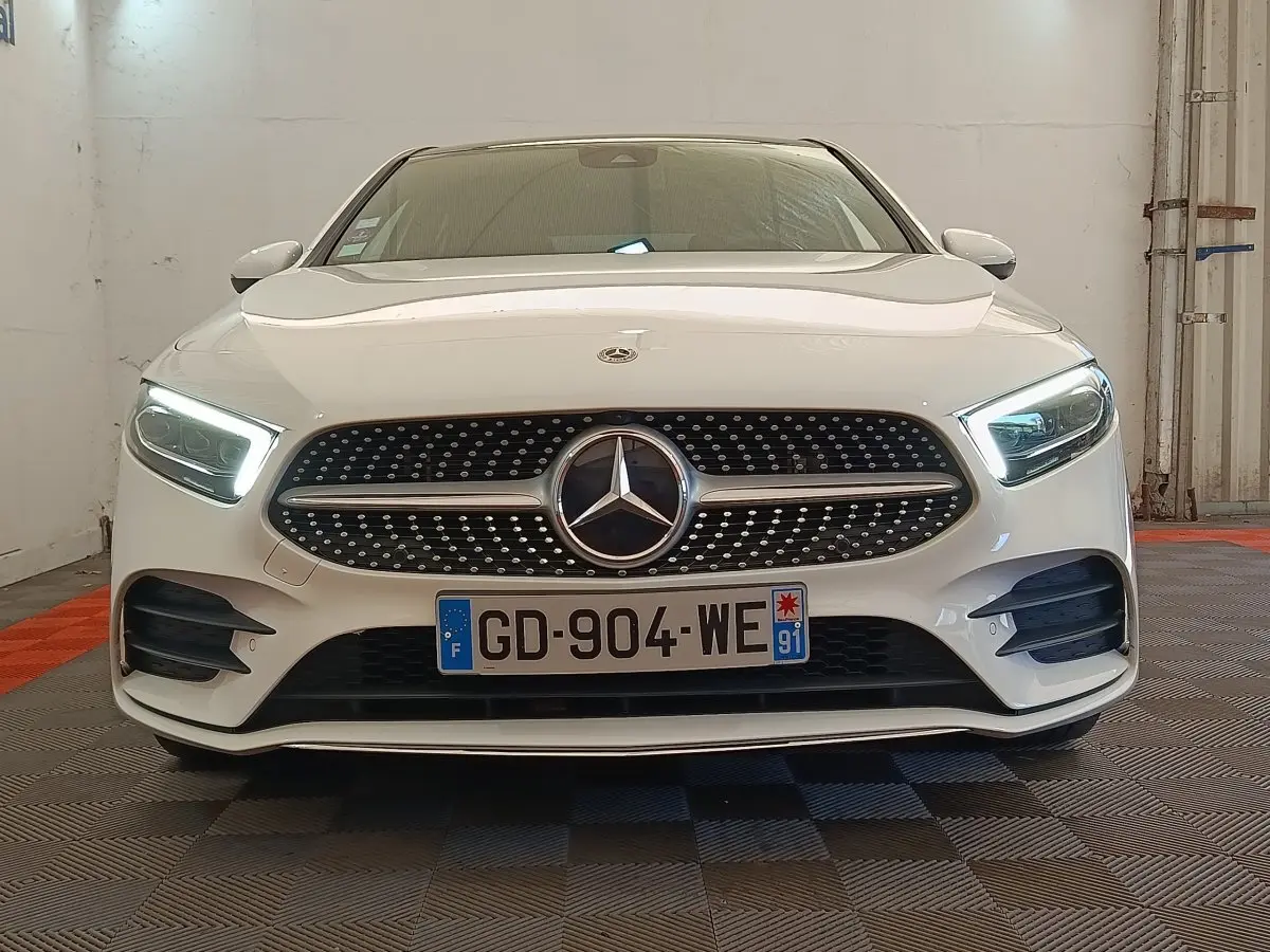 Mercedes Classe A 250 e AMG Line blanche vue de face, phares LED allumés et calandre diamantée distinctive.