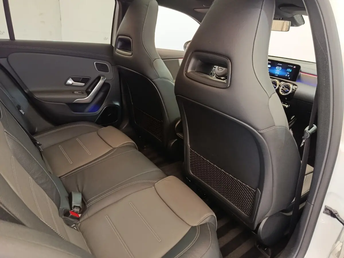 Vue intérieure arrière droite de la Mercedes Classe A 250 e AMG Line blanche, sièges en cuir noir et tableau de bord digital.