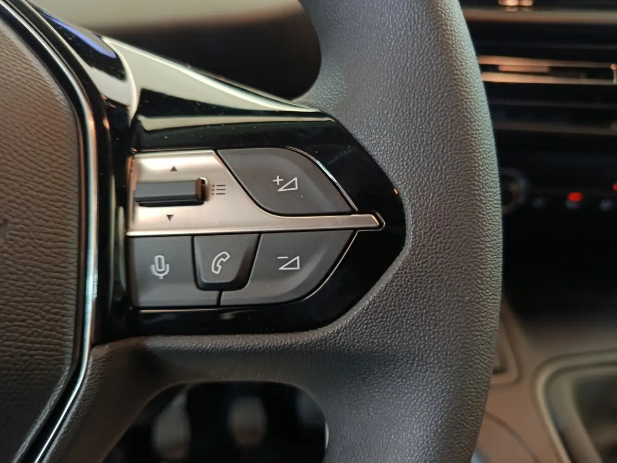 Gros plan sur les commandes vocales et téléphone au volant du Peugeot Partner blanc 2026, intérieur sombre.
