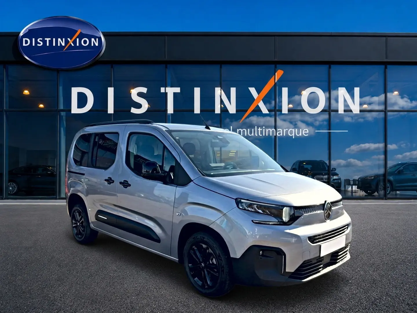 Vue 3/4 avant droite d'un Citroën Berlingo gris acier avec jantes noires devant un showroom Distinxion.