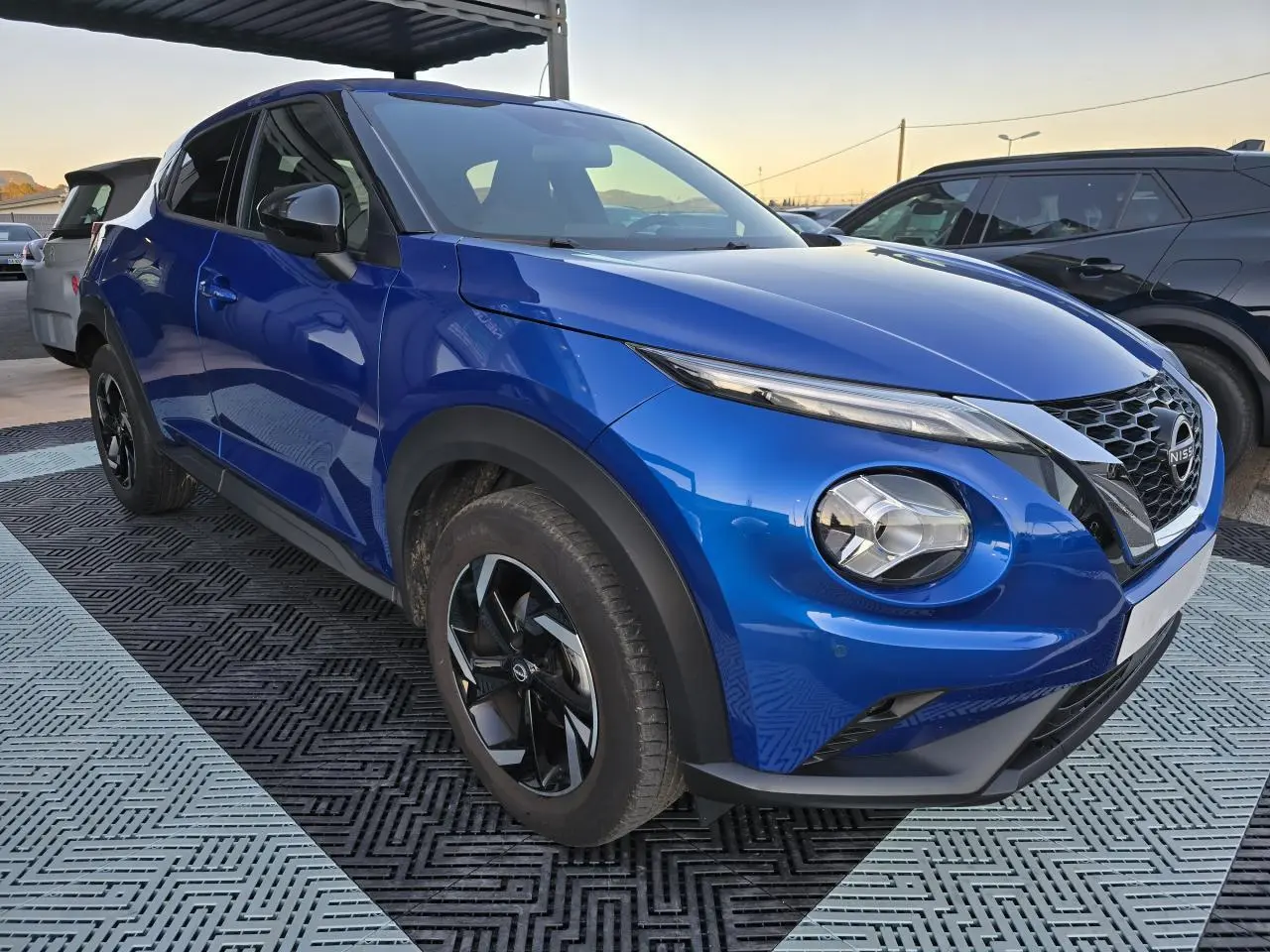 Nissan Juke II bleu magnetic en vue 3/4 avant droit, avec jantes alliage noires et calandre V-Motion distinctive.