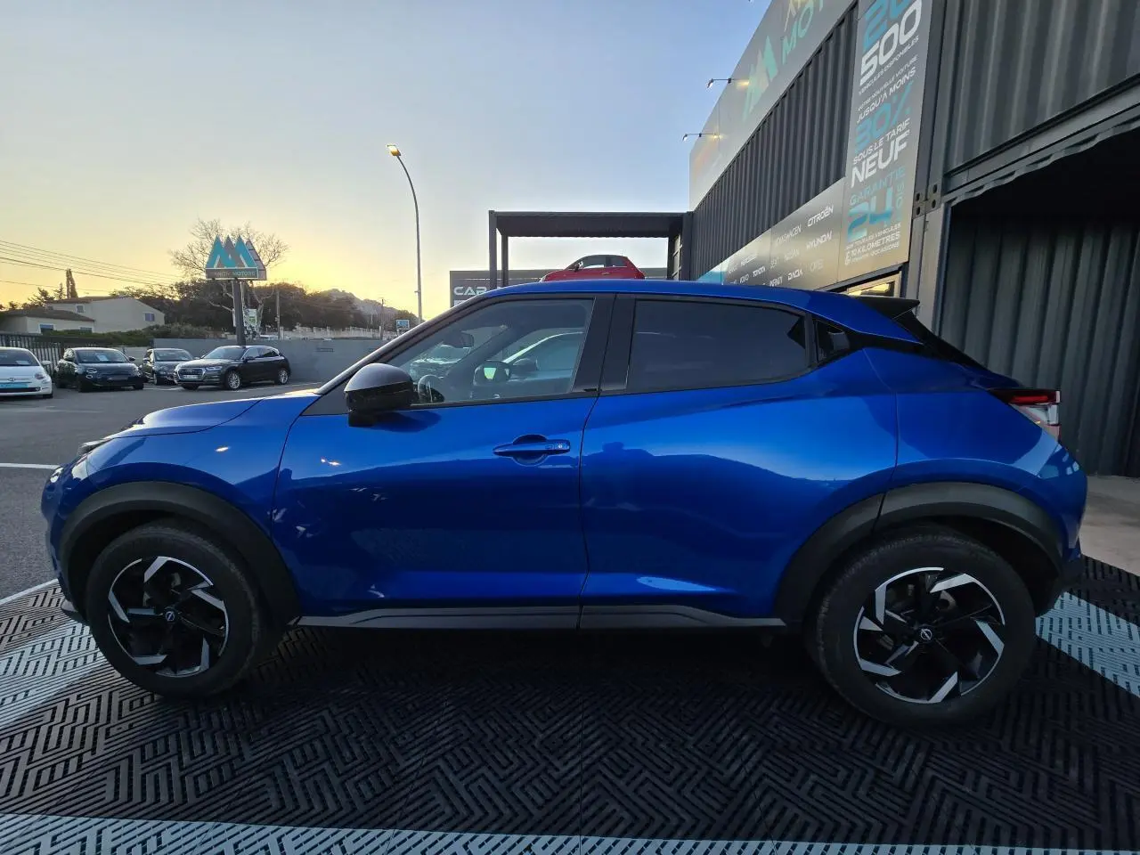 Profil côté gauche d'un Nissan Juke II bleu magnetic avec jantes alliage noires et vitres teintées.