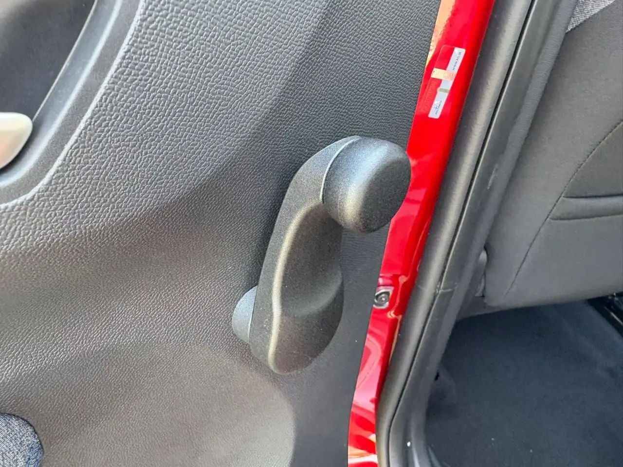 Poignée de lève-vitre manuel côté arrière gauche sur porte rouge Elixir d'une Citroën C3 IV New 2025.