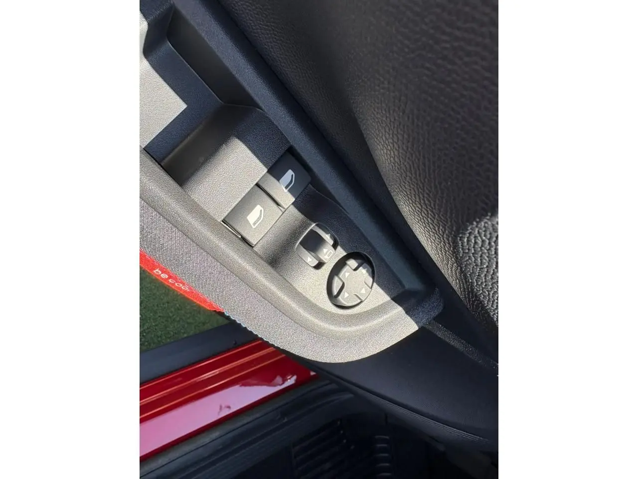 Gros plan sur les commandes de lève-vitres et rétroviseurs côté gauche d'une Citroën C3 rouge Elixir avec intérieur noir.