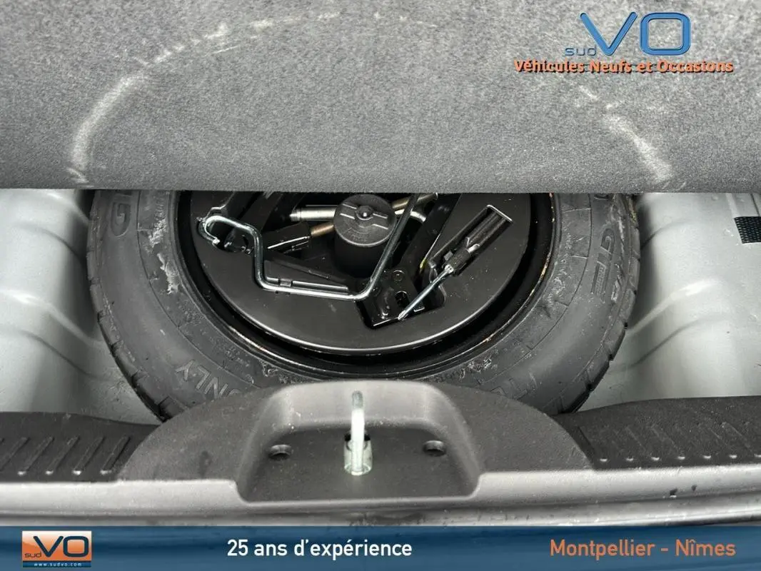 Roue de secours noire avec outils de changement visible dans le coffre d'une FIAT 500C 2024 noire hybride.