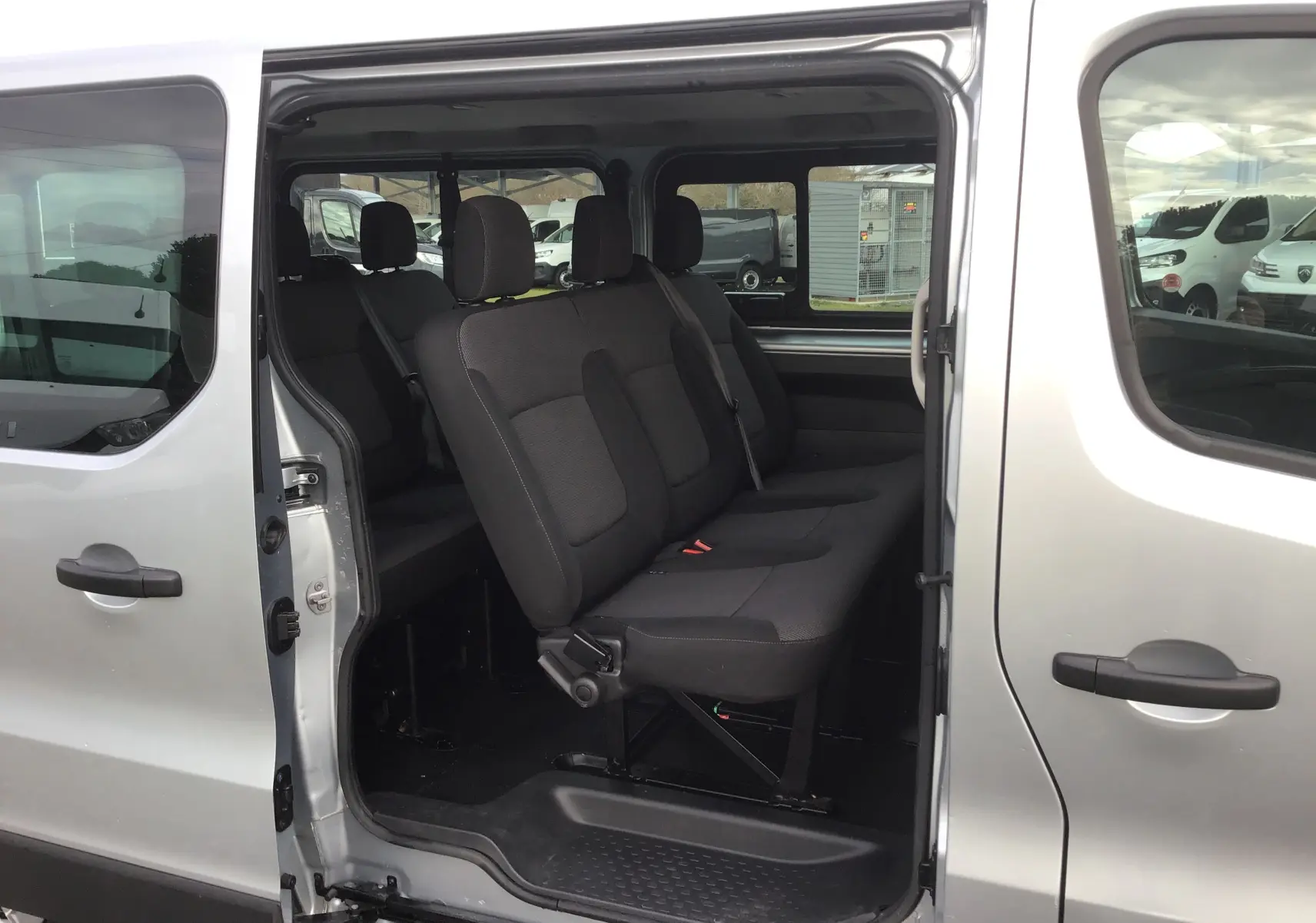 Vue latérale droite du Renault Trafic Combi gris Highland 2022, porte coulissante ouverte montrant les sièges passagers noirs.