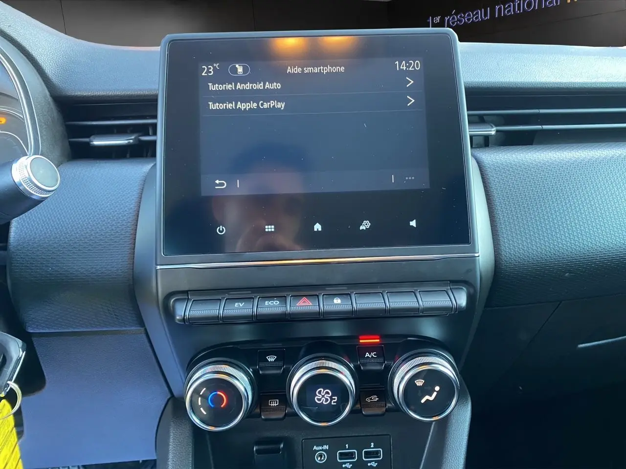 Tableau de bord de Renault Clio V blanc, vue frontale centrée sur l'écran tactile et les commandes de climatisation.