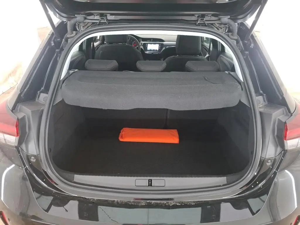 Coffre ouvert vu de l'arrière d'une Opel Corsa Noir Perla 2023, avec cache-bagages et un objet orange à l'intérieur.