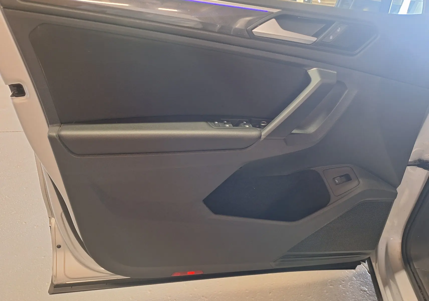 Porte avant gauche ouverte du Volkswagen Tiguan gris, montrant la garniture intérieure noire avec commandes électriques.