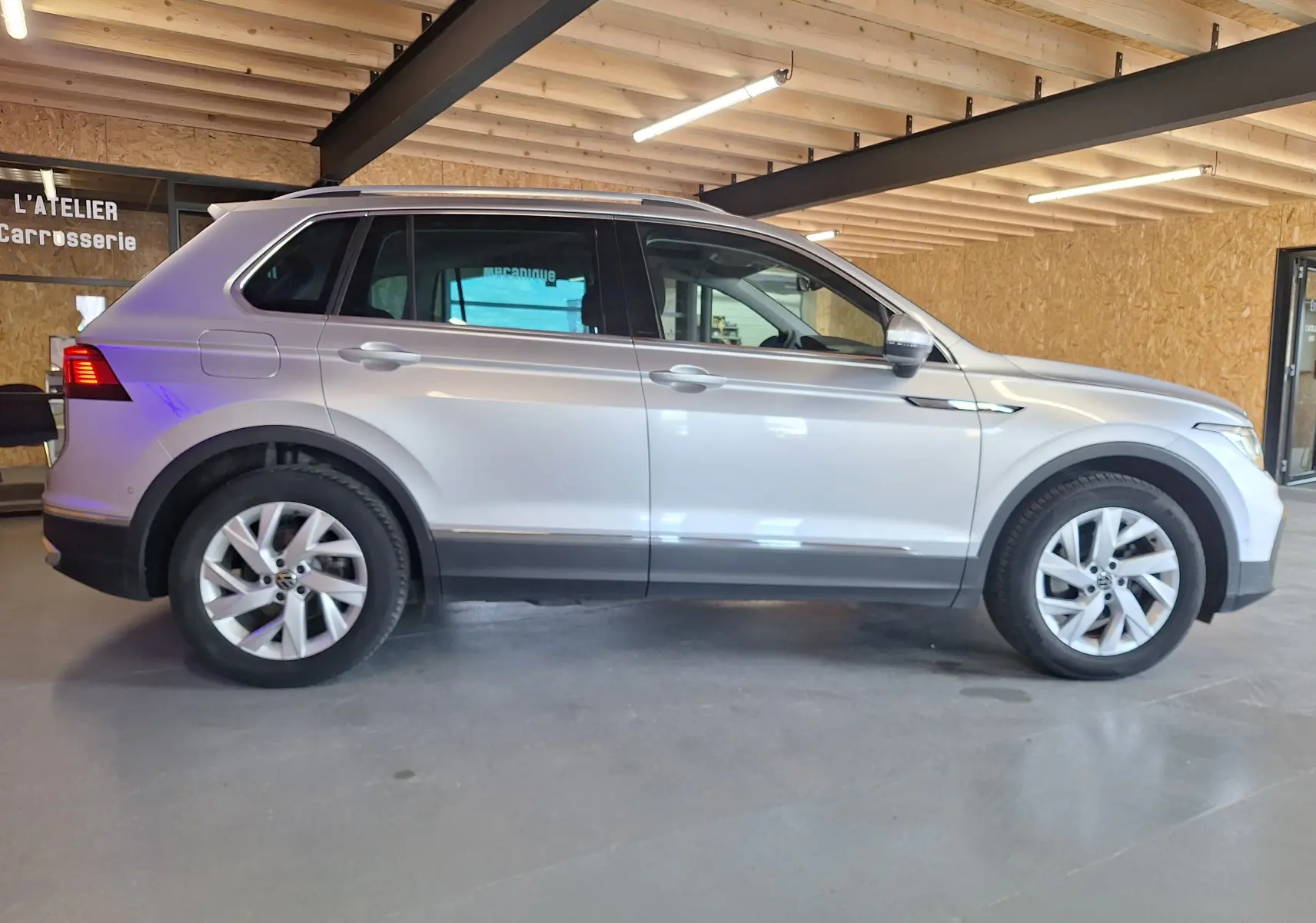 Profil droit du Volkswagen Tiguan gris métallisé 2021 avec jantes alliage 18 pouces et jupes latérales chromées dans un atelier.