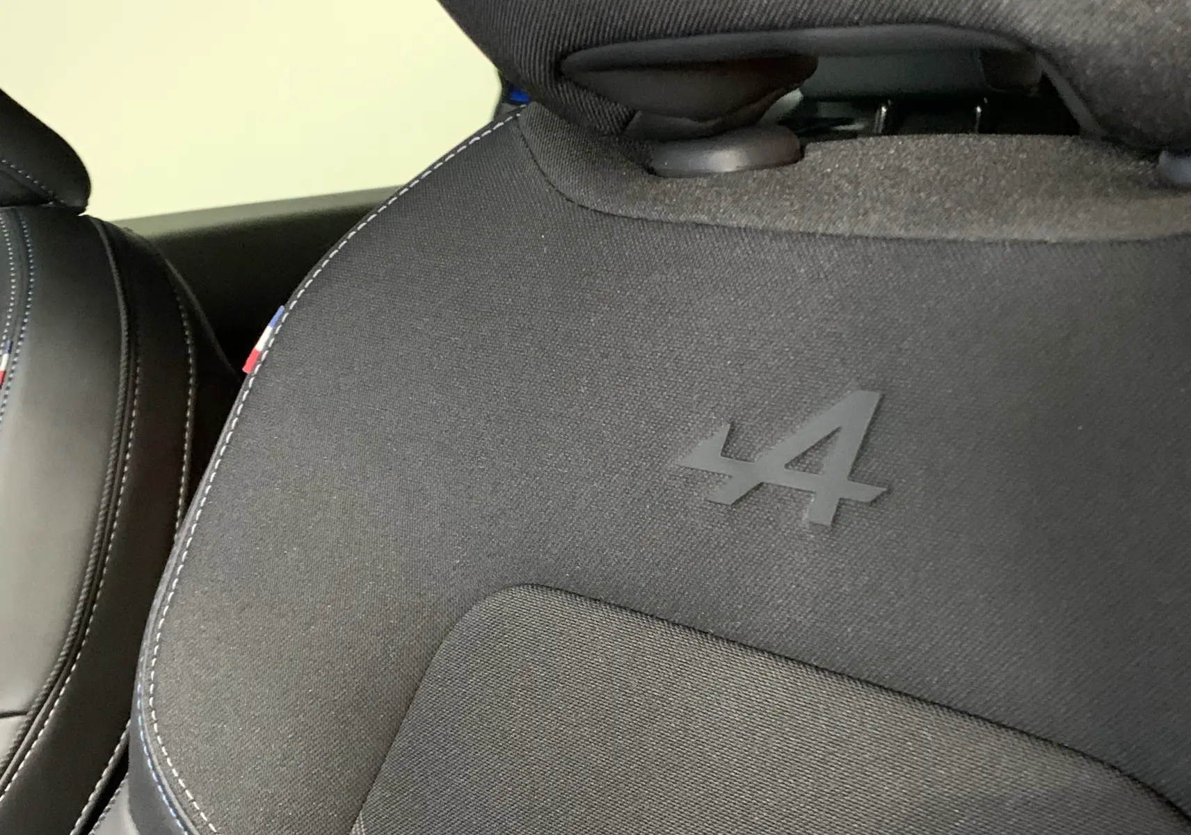 Détail du siège avant en tissu noir avec logo Alpine embossé et surpiqûres bleues sur Renault Symbioz hybride 2025.