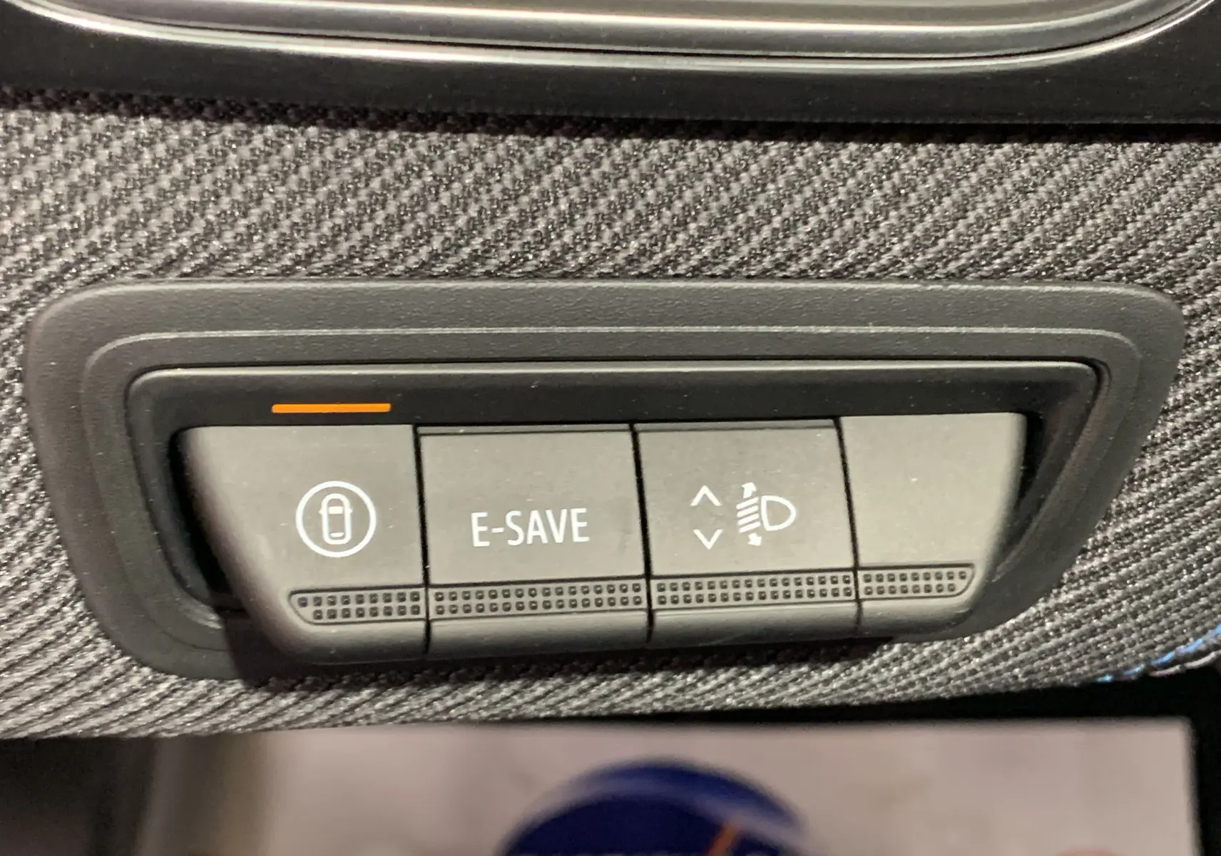 Gros plan sur les boutons de contrôle E-SAVE et réglage des phares sur la planche de bord en tissu du Renault Symbioz bleu iron.