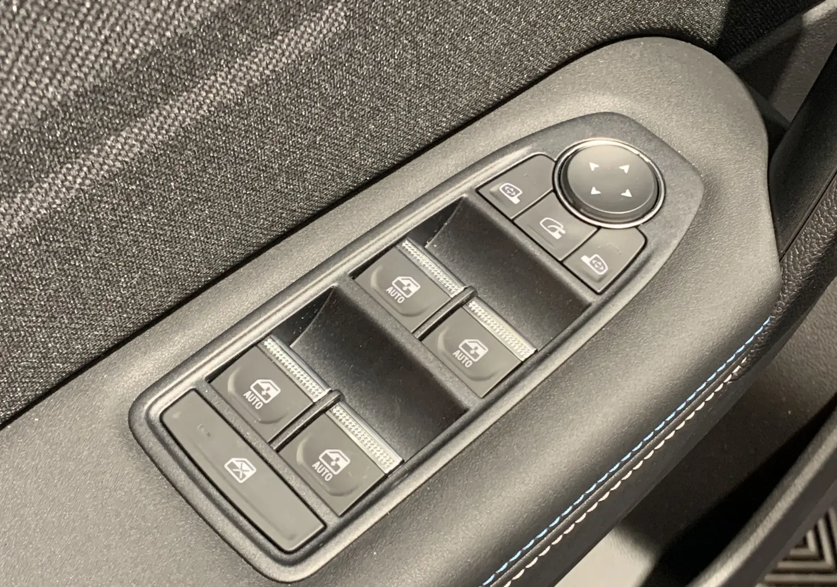 Gros plan sur les commandes de lève-vitres et rétroviseurs avec surpiqûres bleues dans une Renault Symbioz Bleu Iron.