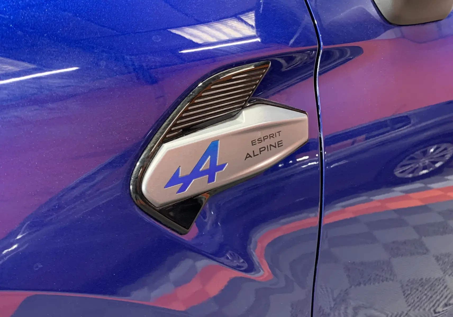 Gros plan sur l'aile avant gauche bleu iron du Renault Symbioz 2025 avec logo Esprit Alpine bleu et argent.